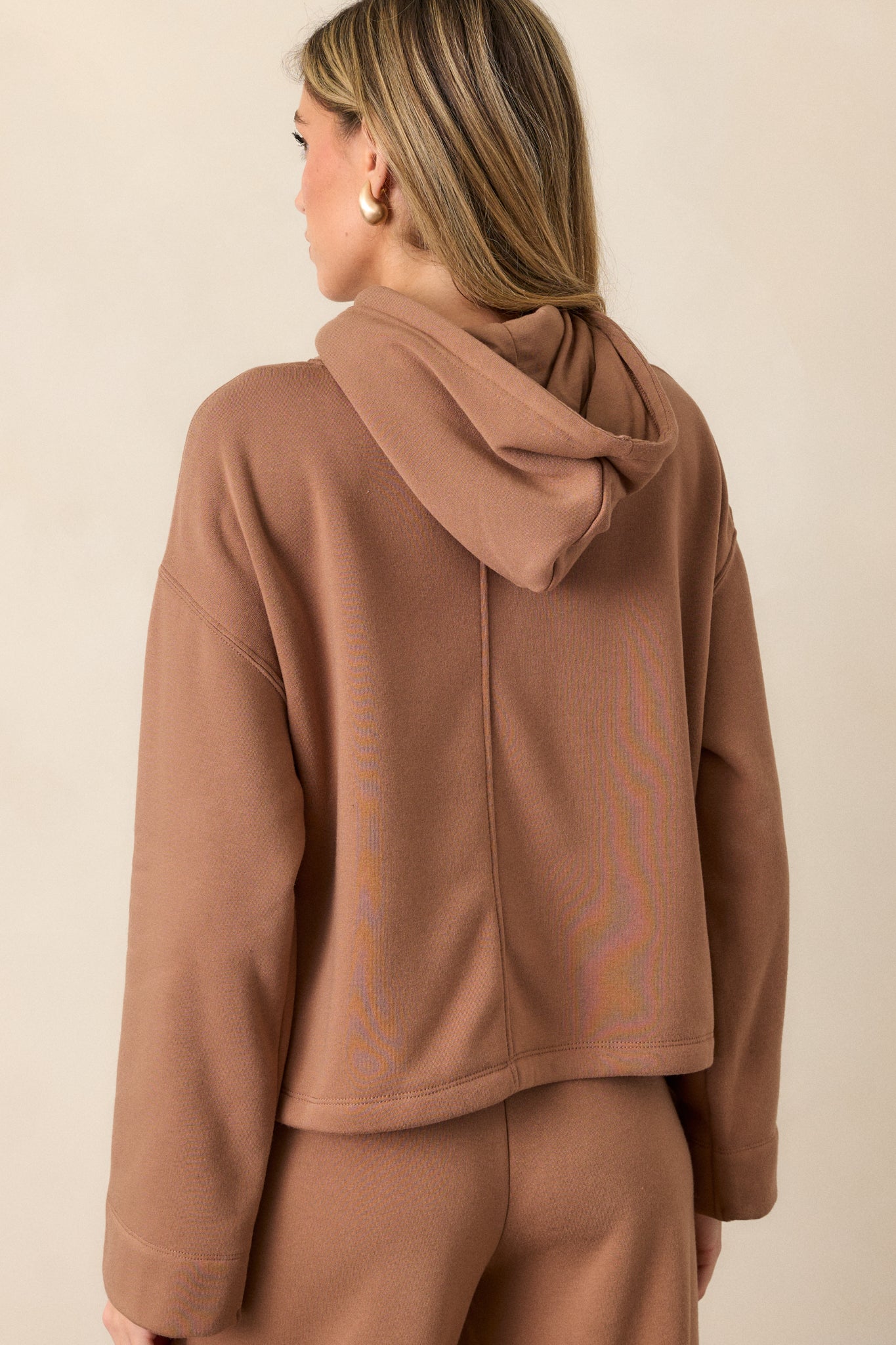 Back view of the brown sweatshirt, showing the relaxed fit of the hood and loose sleeves from behind.