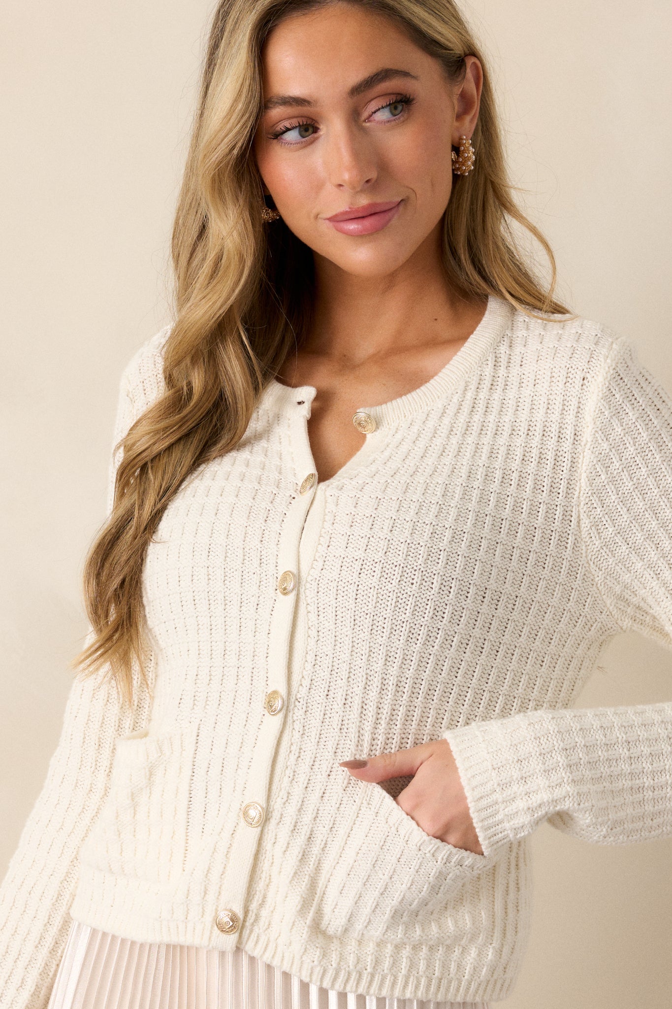 Angled view of the ivory sweater displaying the ribbed knit texture, gold hardware accents, and the functional front pockets.