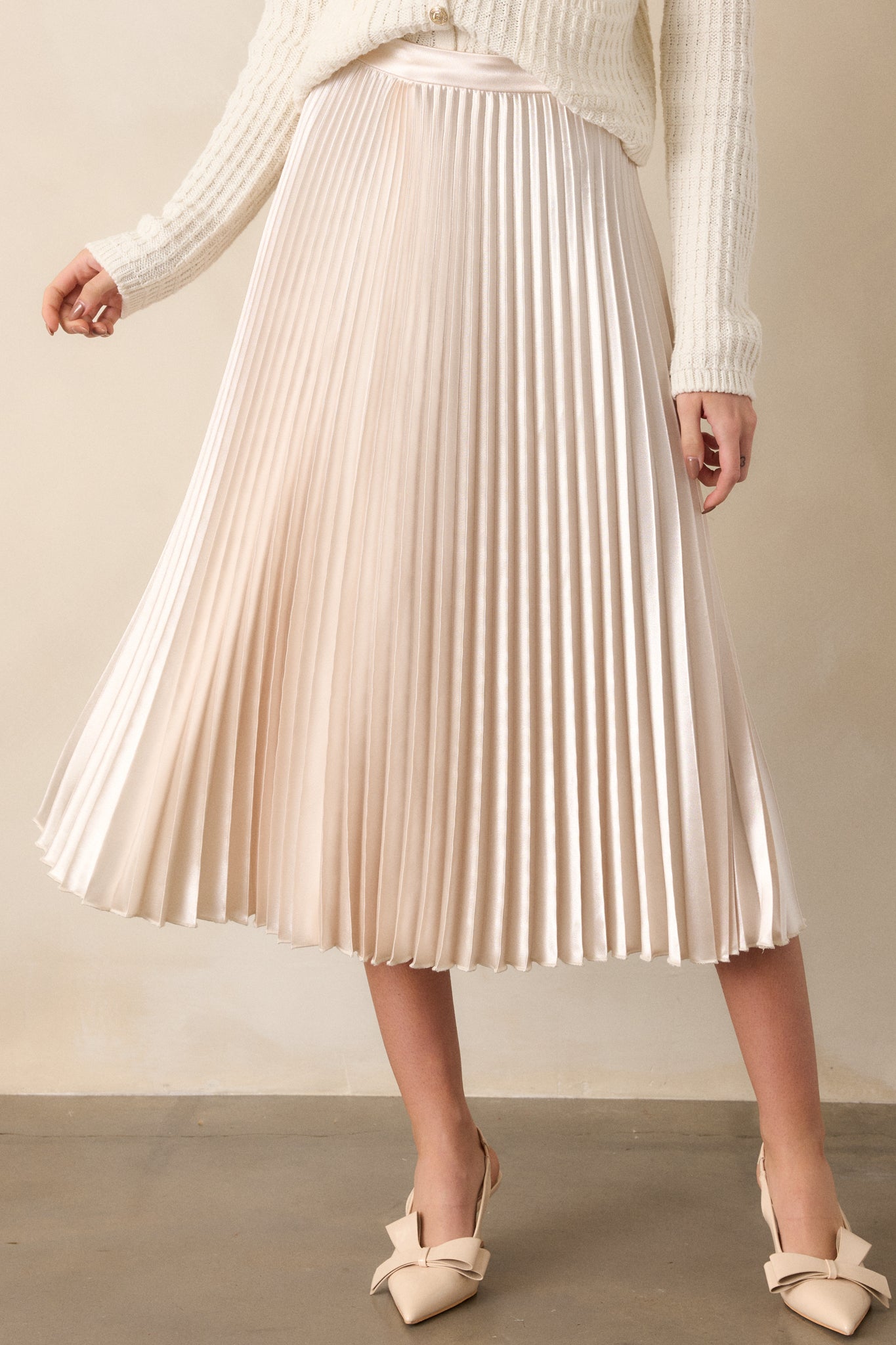 Front view of an ivory midi skirt featuring a high waisted design, an elastic insert at the back of the waist, a discrete side zipper, and heavy pleating throughout.