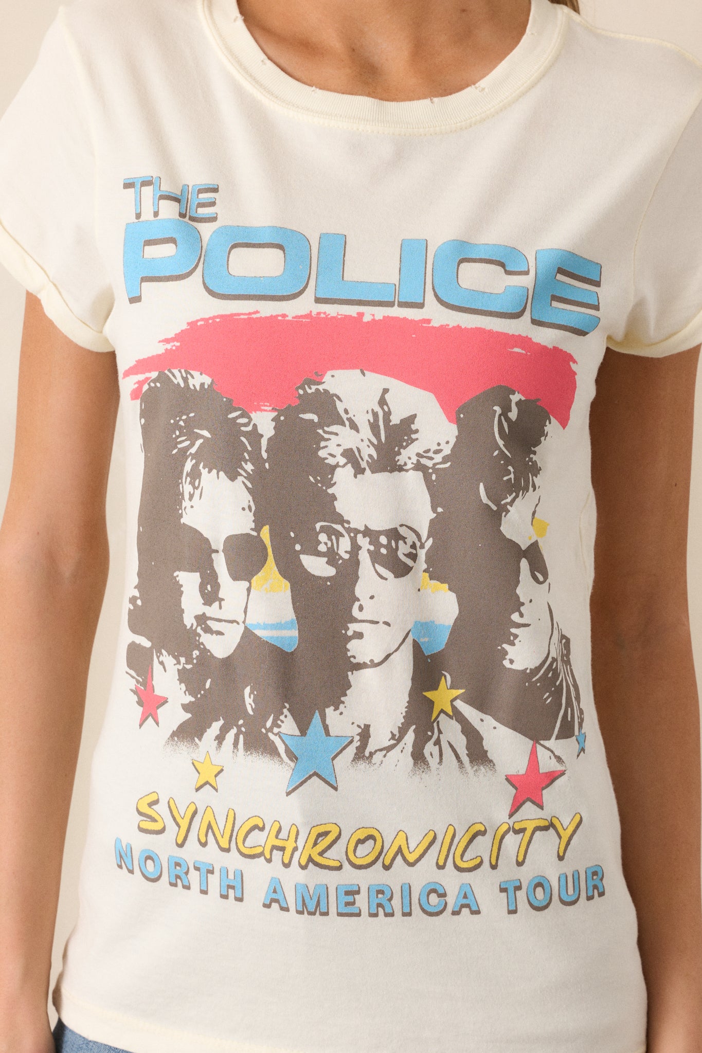 A detailed shot of the graphic on the front of the ivory tee, focusing on the "The Police Synchronicity North America Tour" print. The vintage-style design is visible along with the distressed edges around the neckline and sleeves.