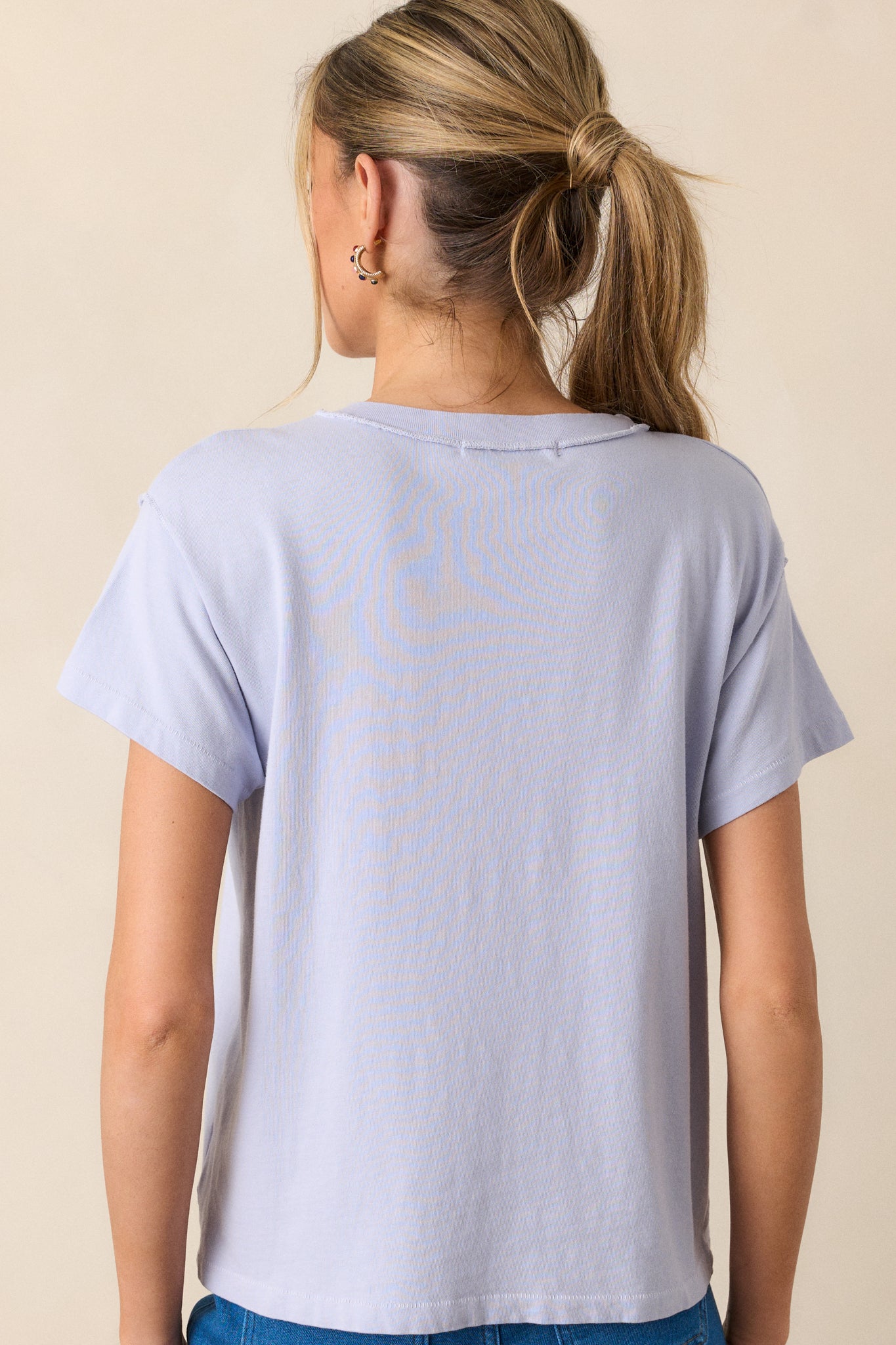 A back view of the lavender top, showing its simple design with no graphic. The short sleeves and round neckline are visible, emphasizing the clean, casual silhouette of the top.