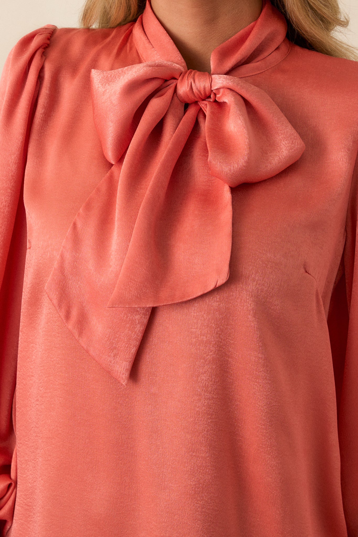 Close-up of the pink coral top showing the high neckline with adjustable self tie, flowy balloon sleeves with two buttons at the cuff, and the texture of the fabric.