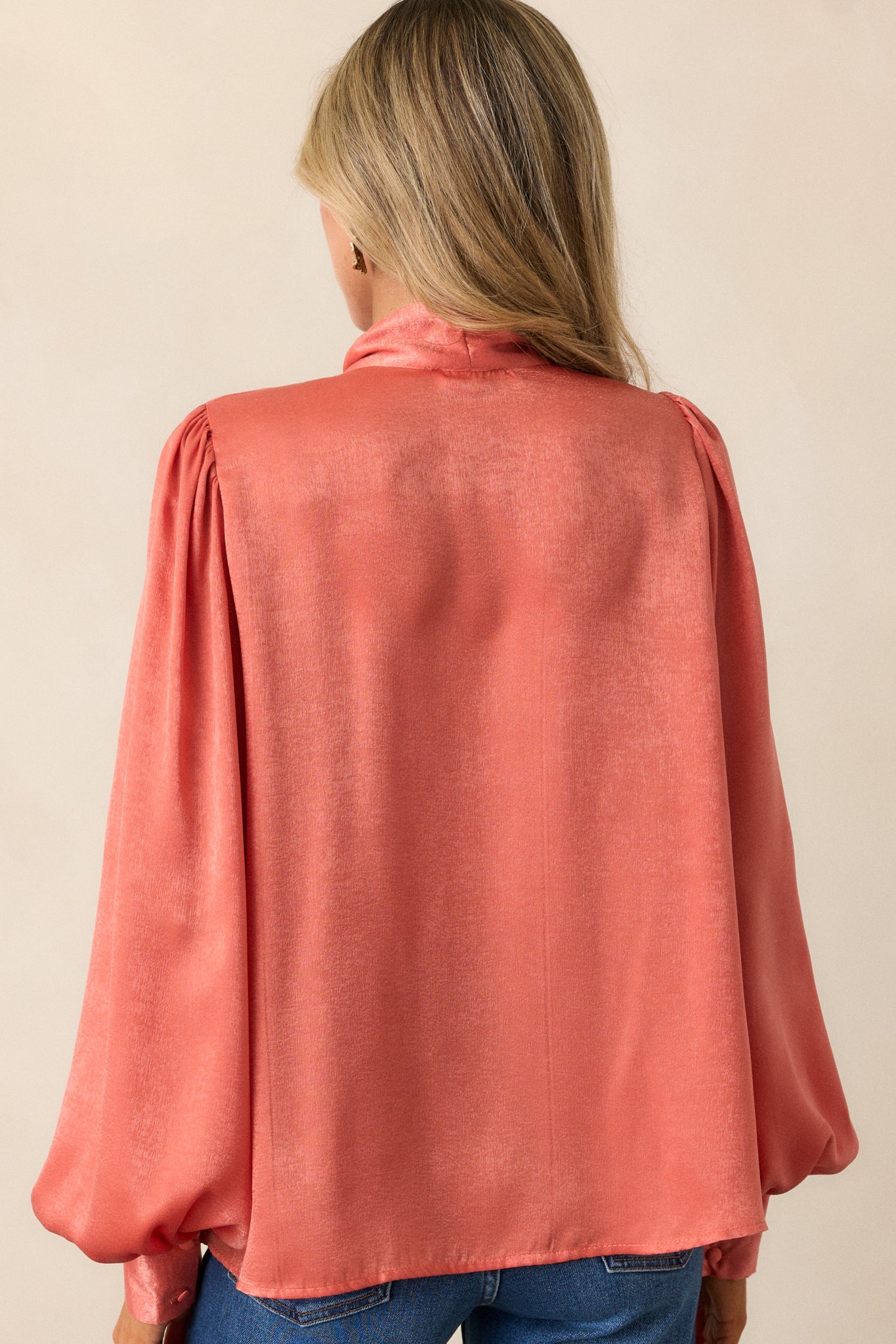 Back view of a pink coral top highlighting the high neckline with self tie and the flowy balloon sleeves.