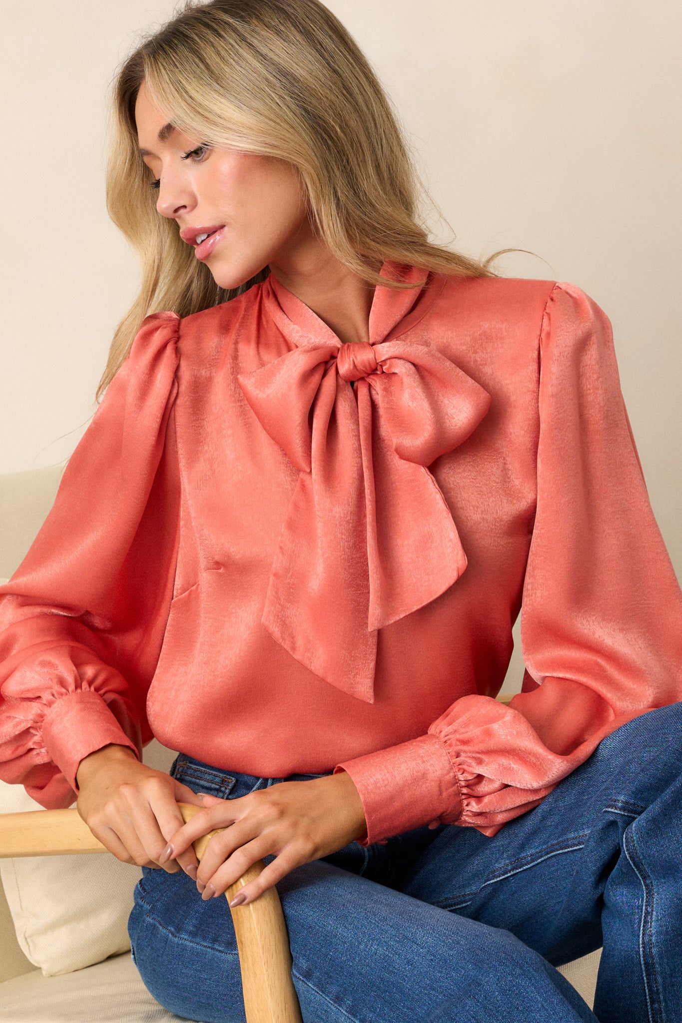 This pink coral top features a high neckline with an adjustable self tie, flowy balloon sleeves with two buttons at the cuff, and a relaxed fit.