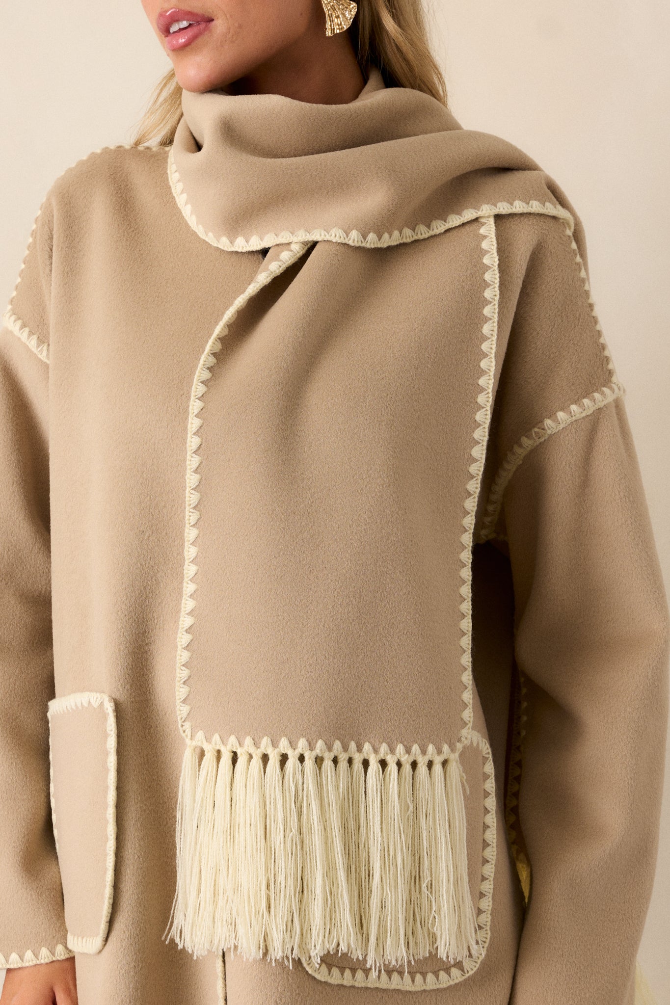 Close up of the blanket stitching on this taupe coat and scarf with fringe detailing. 