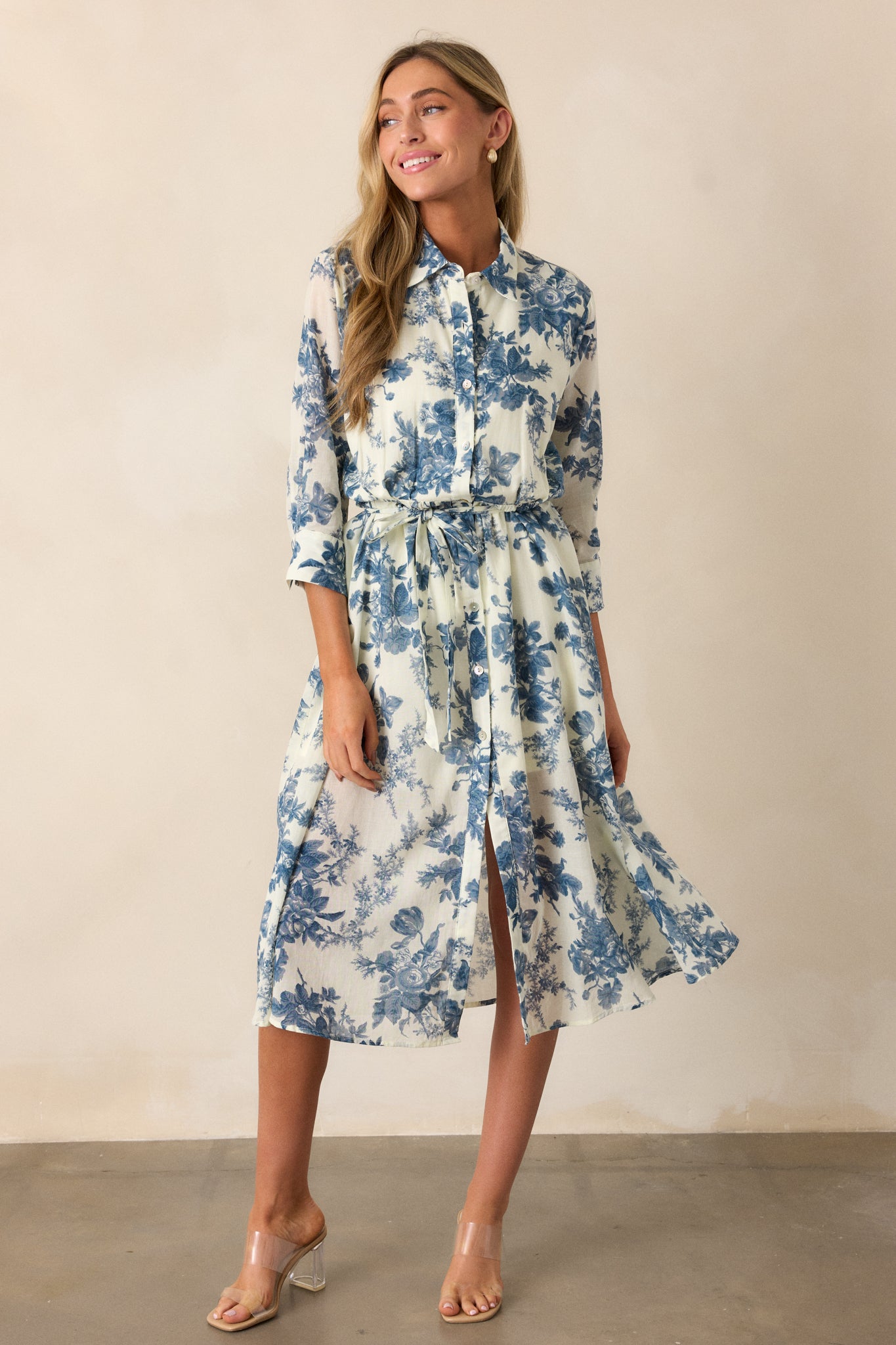 A full view of the blue midi dress, showcasing the collared neckline, blue floral pattern, and 3/4 length sleeves with button cuffs.