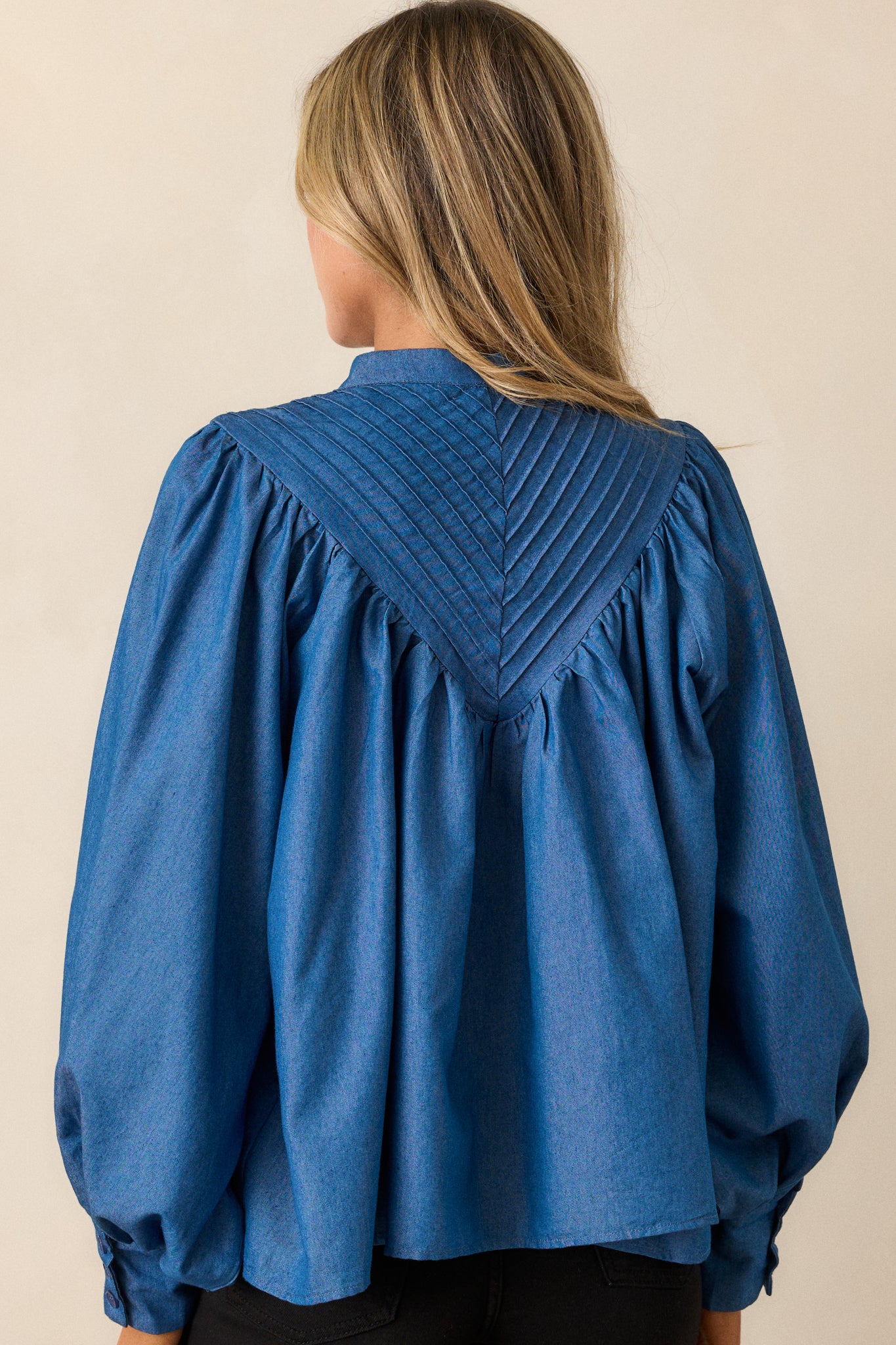 Back view of the denim blouse, displaying the clean lines of the fabric, the long puff sleeves, and the overall relaxed fit.





