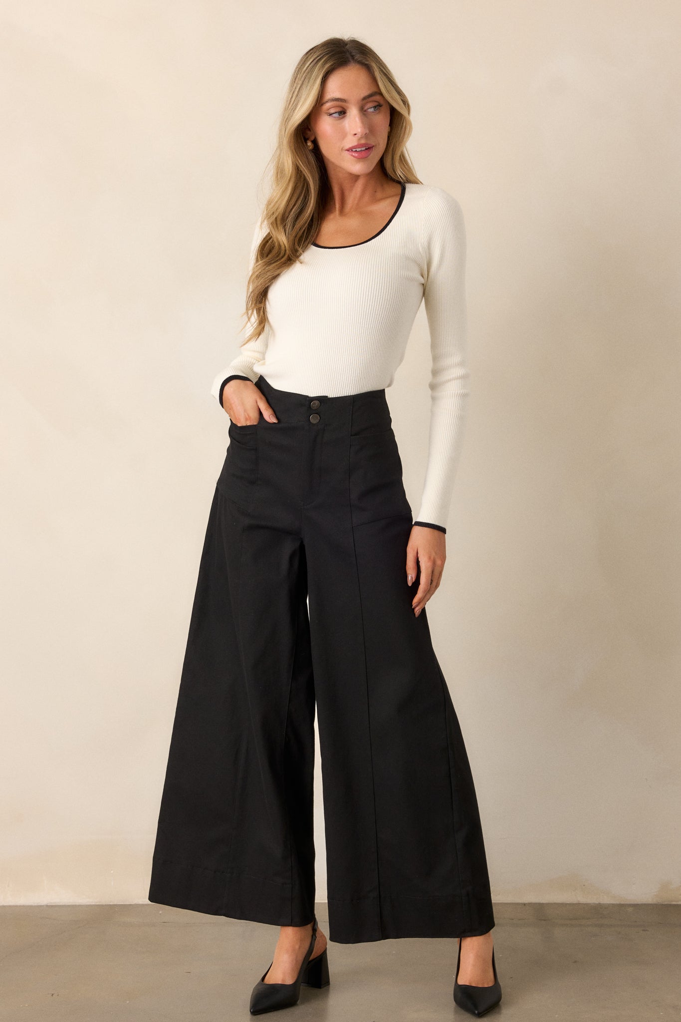 Full length view of black pants showing the button zipper closure and functional rectangular hip pockets.