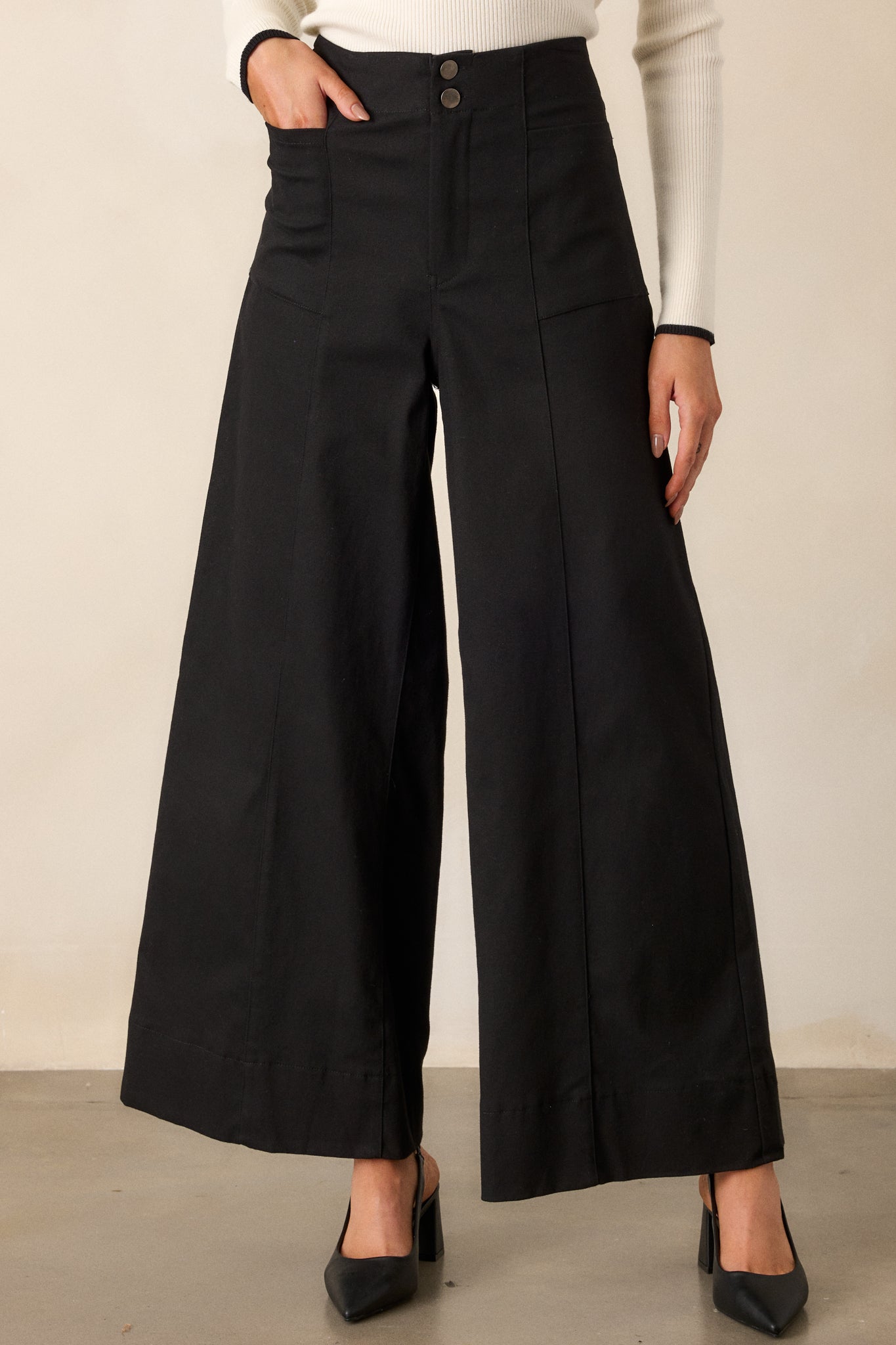 Front view of black pants featuring a high waisted design, a button zipper closure, functional rectangular hip pockets, and a wide leg.