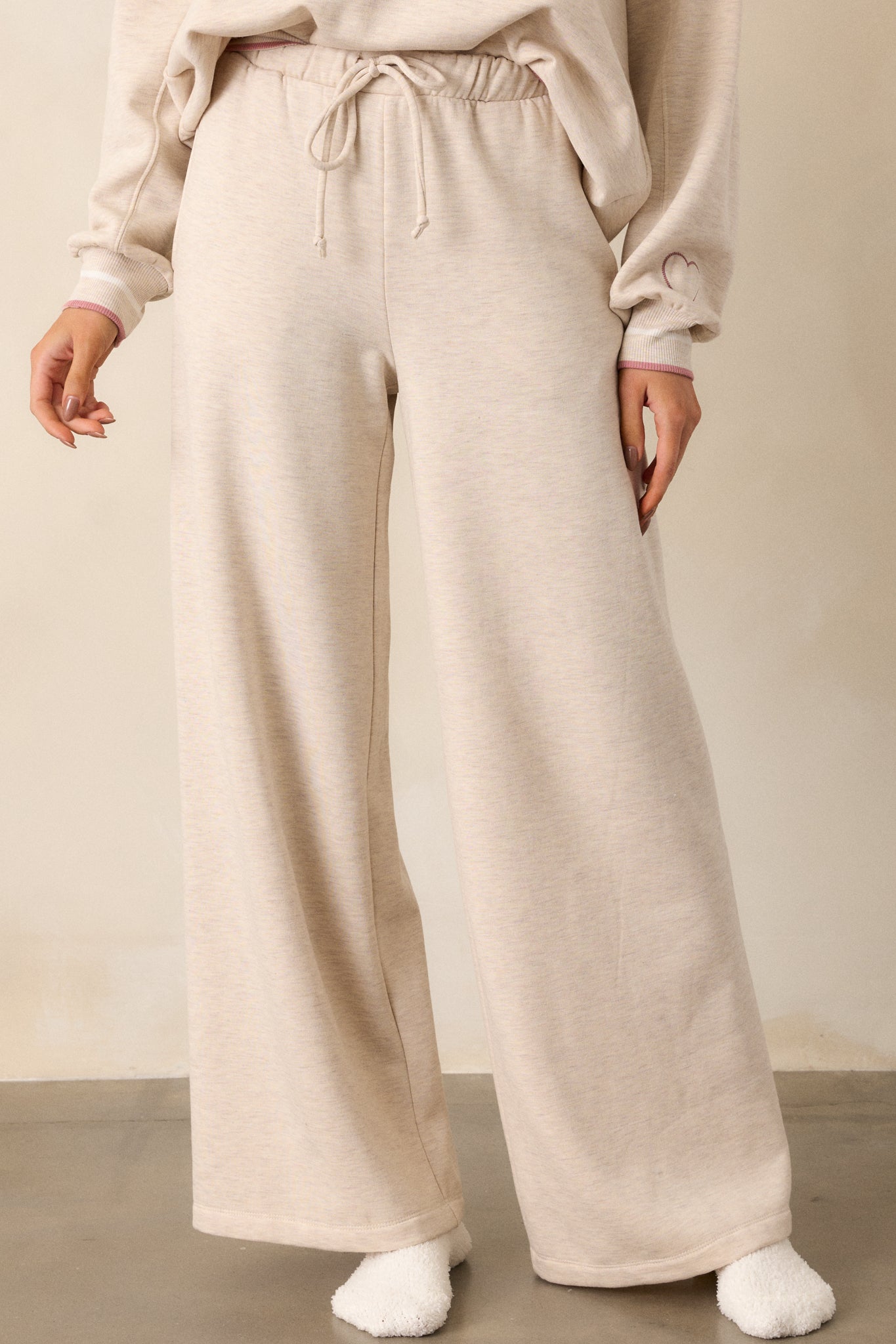 A close-up view of the oatmeal pants from the waist down, emphasizing the soft fleece texture, elastic waistband with self-tie drawstring, and functional hip pockets.