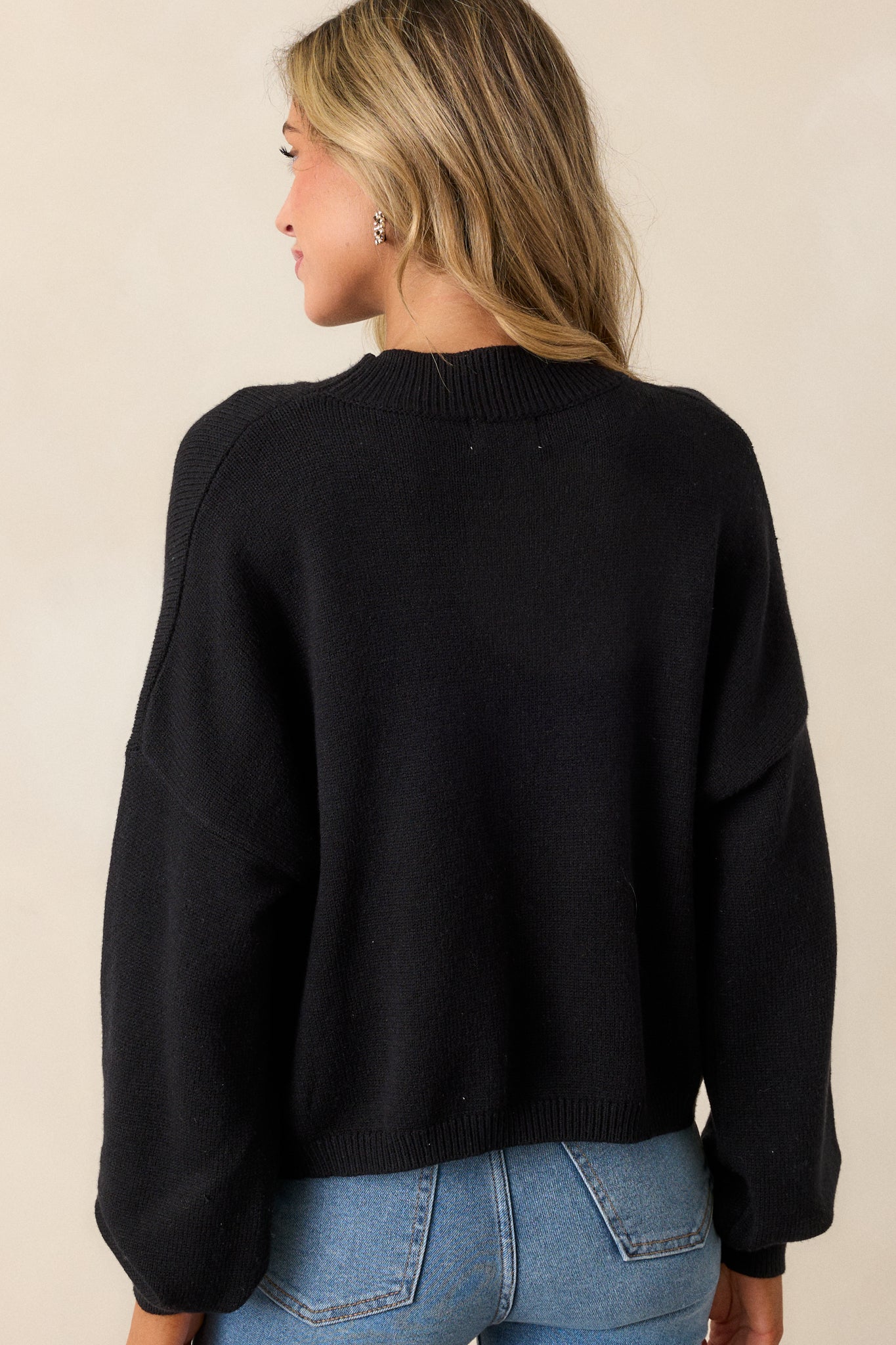 A back view of the sweater, showcasing the smooth fabric and the clean, tapered design at the bottom hem.