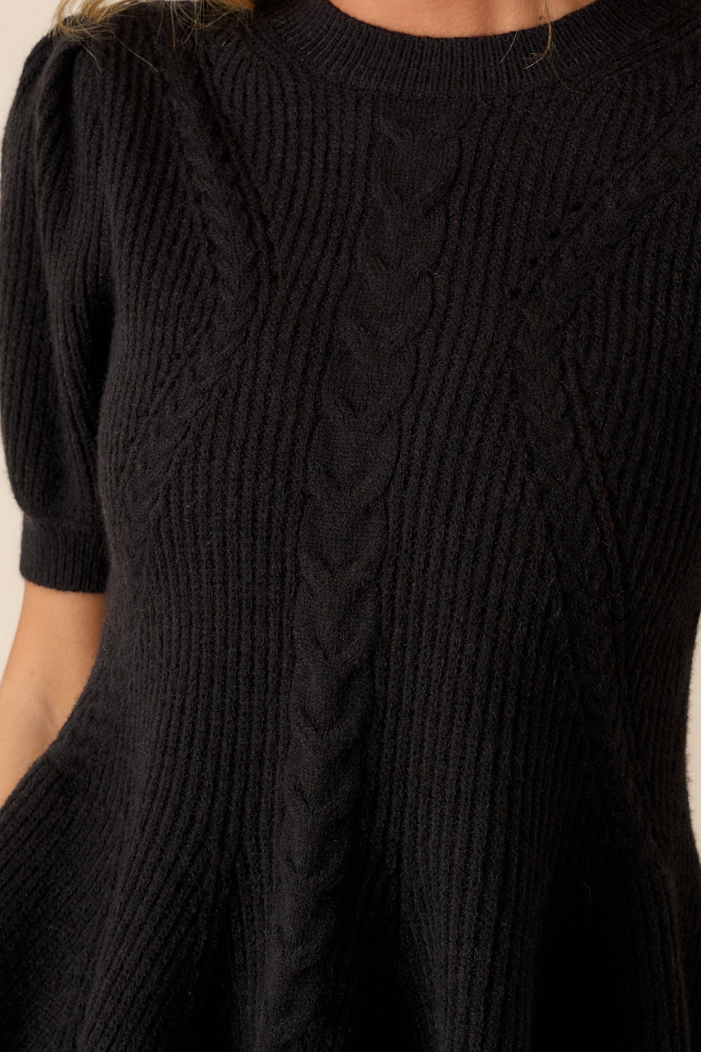 A close-up of the braided knit detailing on the black sweater, with a focus on the ribbed neckline and texture of the fabric.