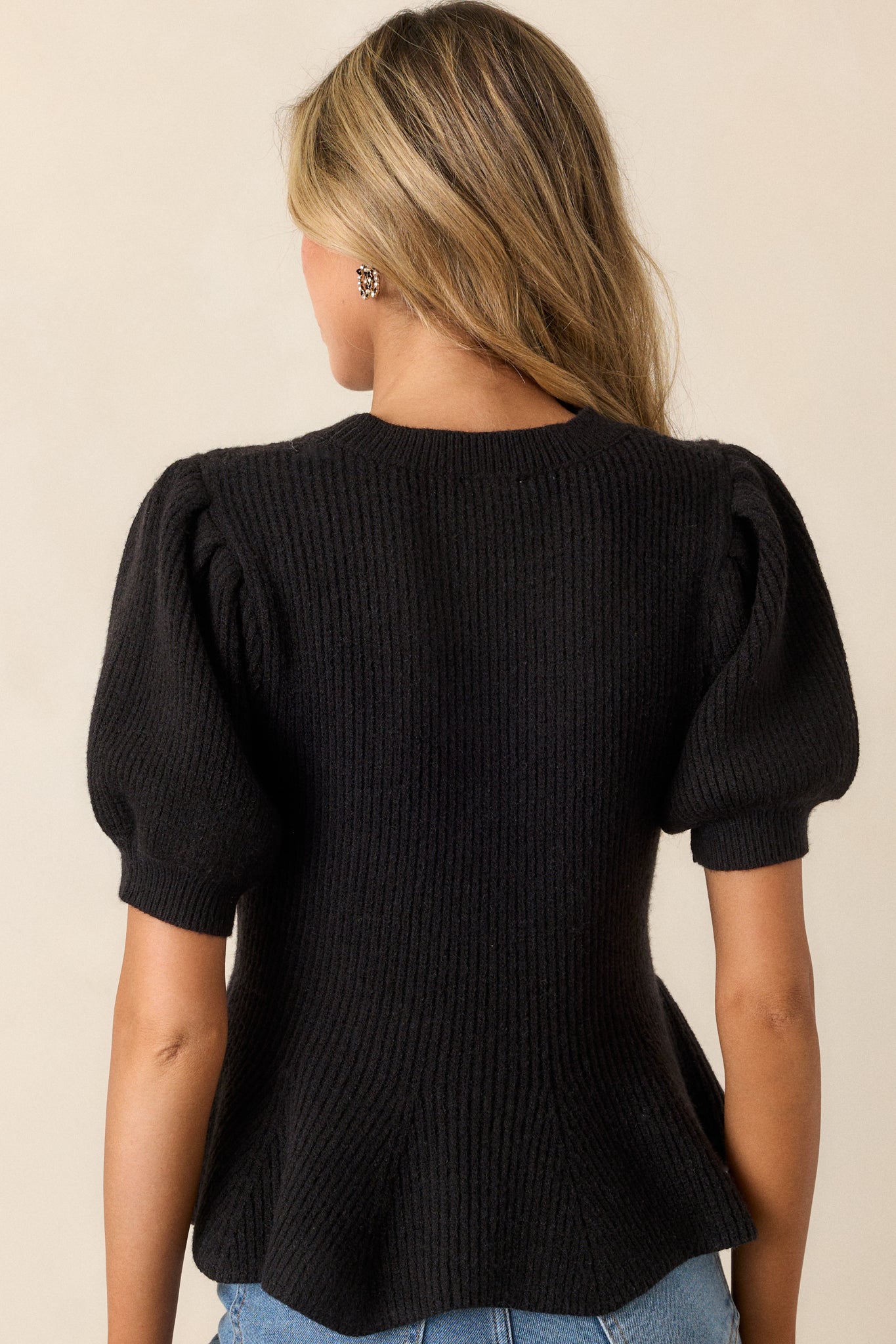 A back view of the black sweater, highlighting the peplum silhouette and puff sleeves with ribbed cuffs.