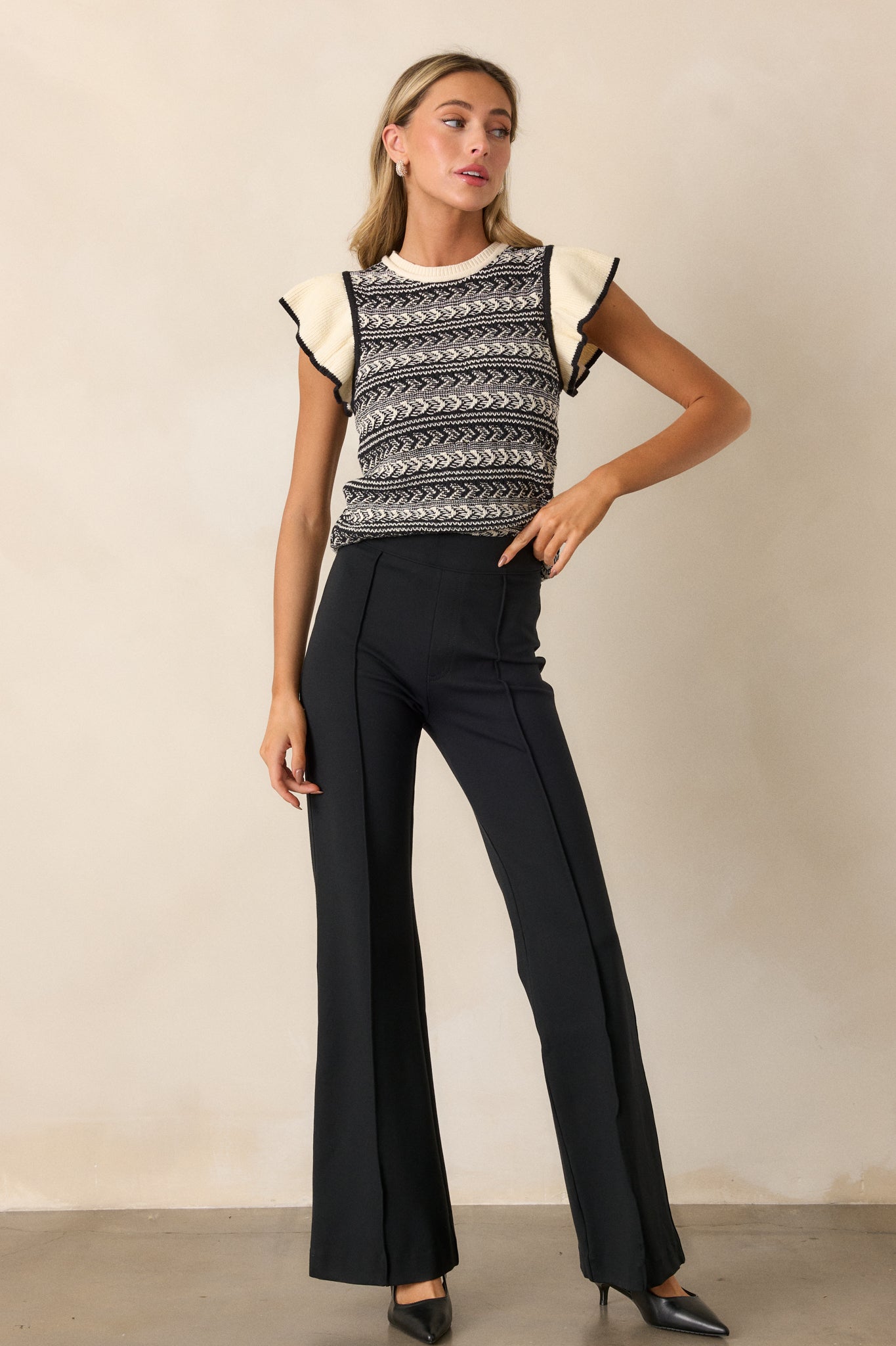 Front view of a black sweater top featuring an ivory rounded neck, a black and white horizontal chevron pattern, a ribbed hemline, and short flutter sleeves with a black trim.