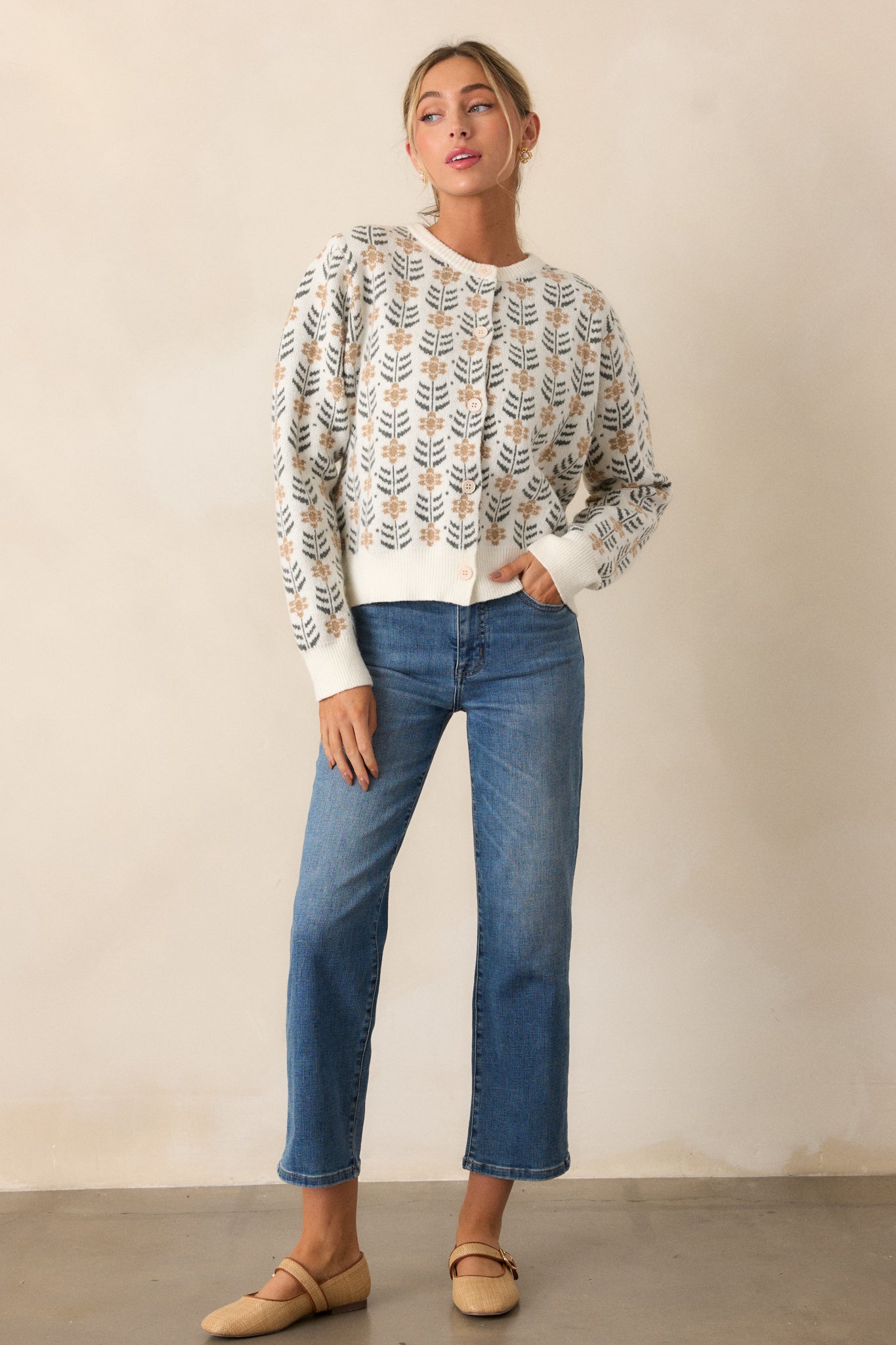 Full body view of an ivory cardigan featuring a round neckline, a repeating pattern of delicate beige floral motifs with dark green leaf accents, ribbed hems and long sleeves.