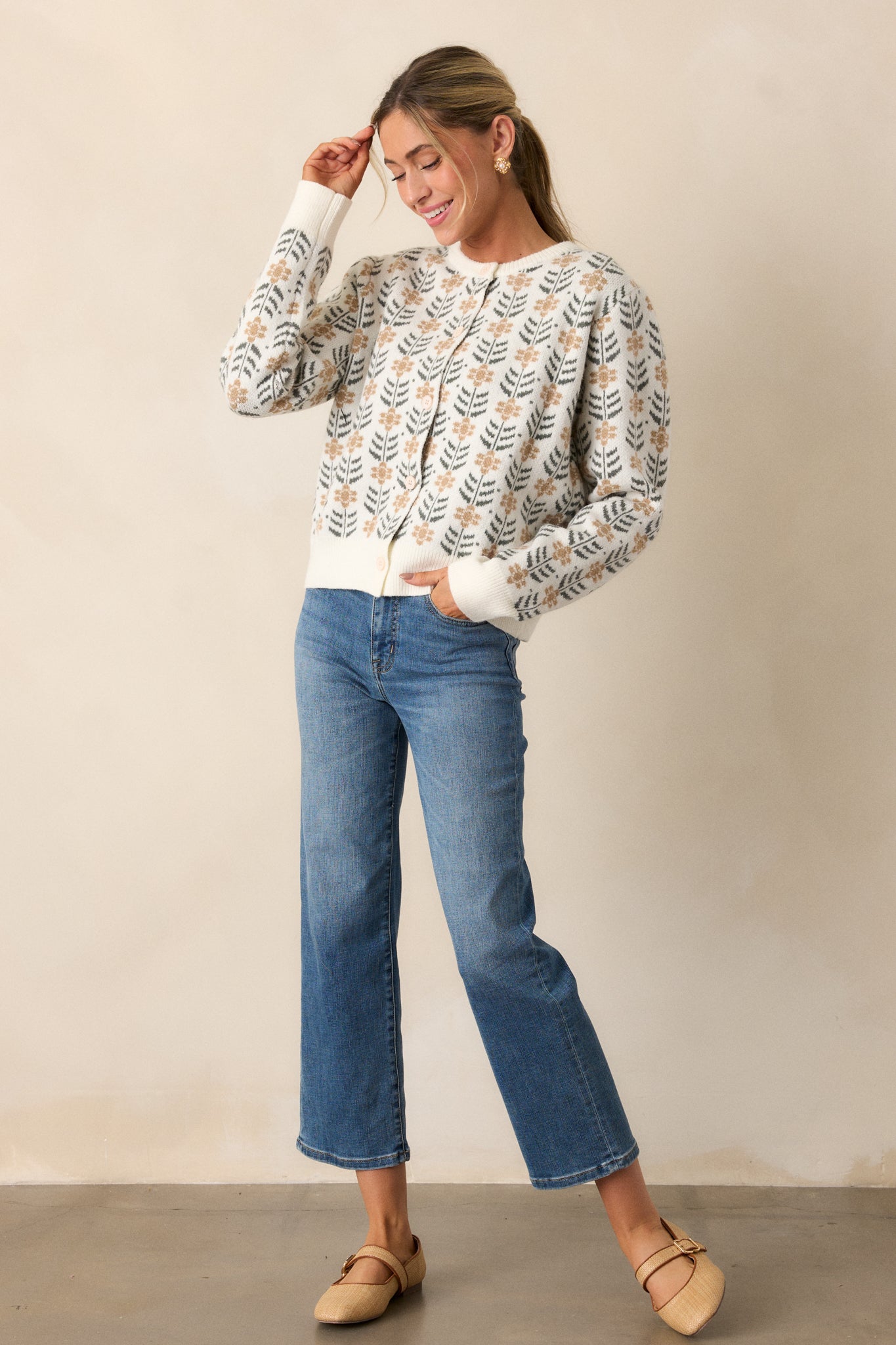 Front view of an ivory cardigan featuring a round neckline, a repeating pattern of delicate beige floral motifs with dark green leaf accents, ribbed hems and long sleeves.