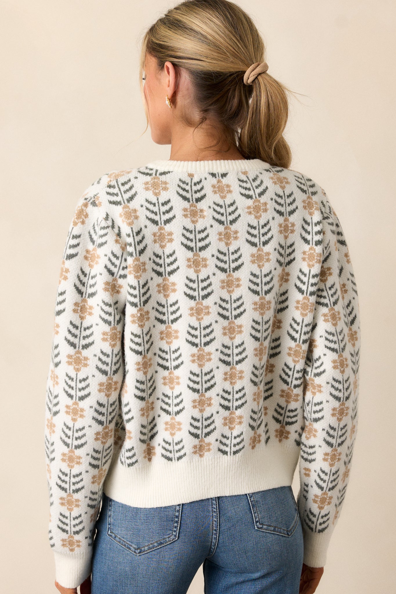 Back view of an ivory cardigan featuring a round neckline, a repeating pattern of delicate beige floral motifs with dark green leaf accents, ribbed hems and long sleeves.