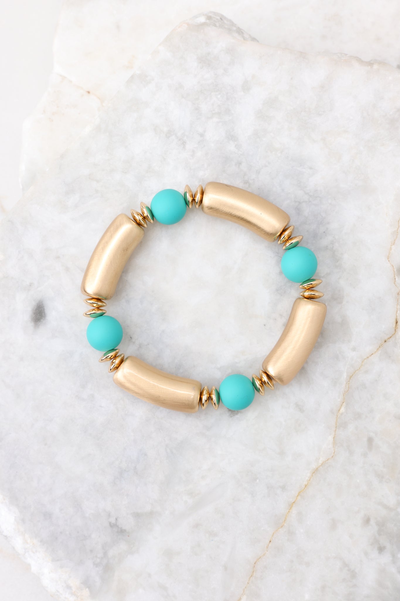 Overhead view of bracelet that features alternating gold and teal beads and measures approximately 2.5" in diameter.  