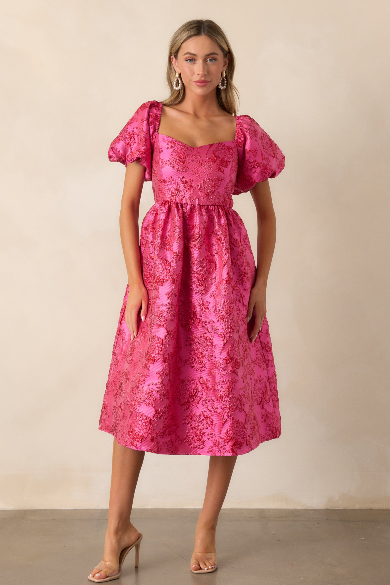 Front view of the pink midi dress showcasing a sweetheart neckline, puff sleeves, and the fit and flare design with sparkle red detailing throughout.