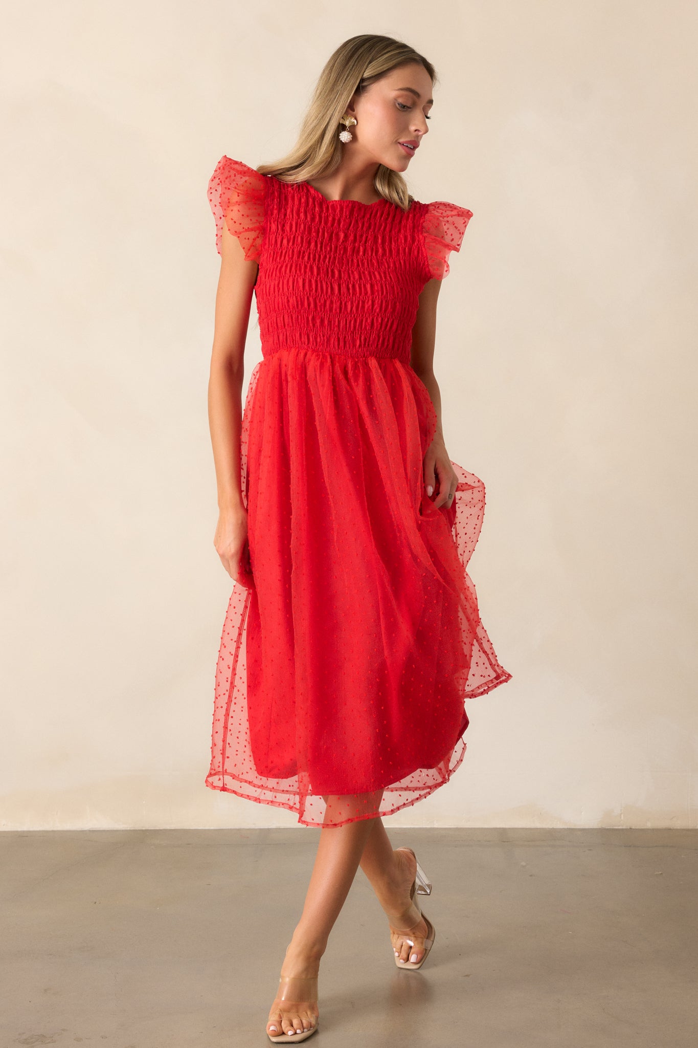 A full-length view of the red dress, highlighting the flutter sleeves and the soft, flowing silhouette created by the polka dot tulle overlay over the smocked bodice.