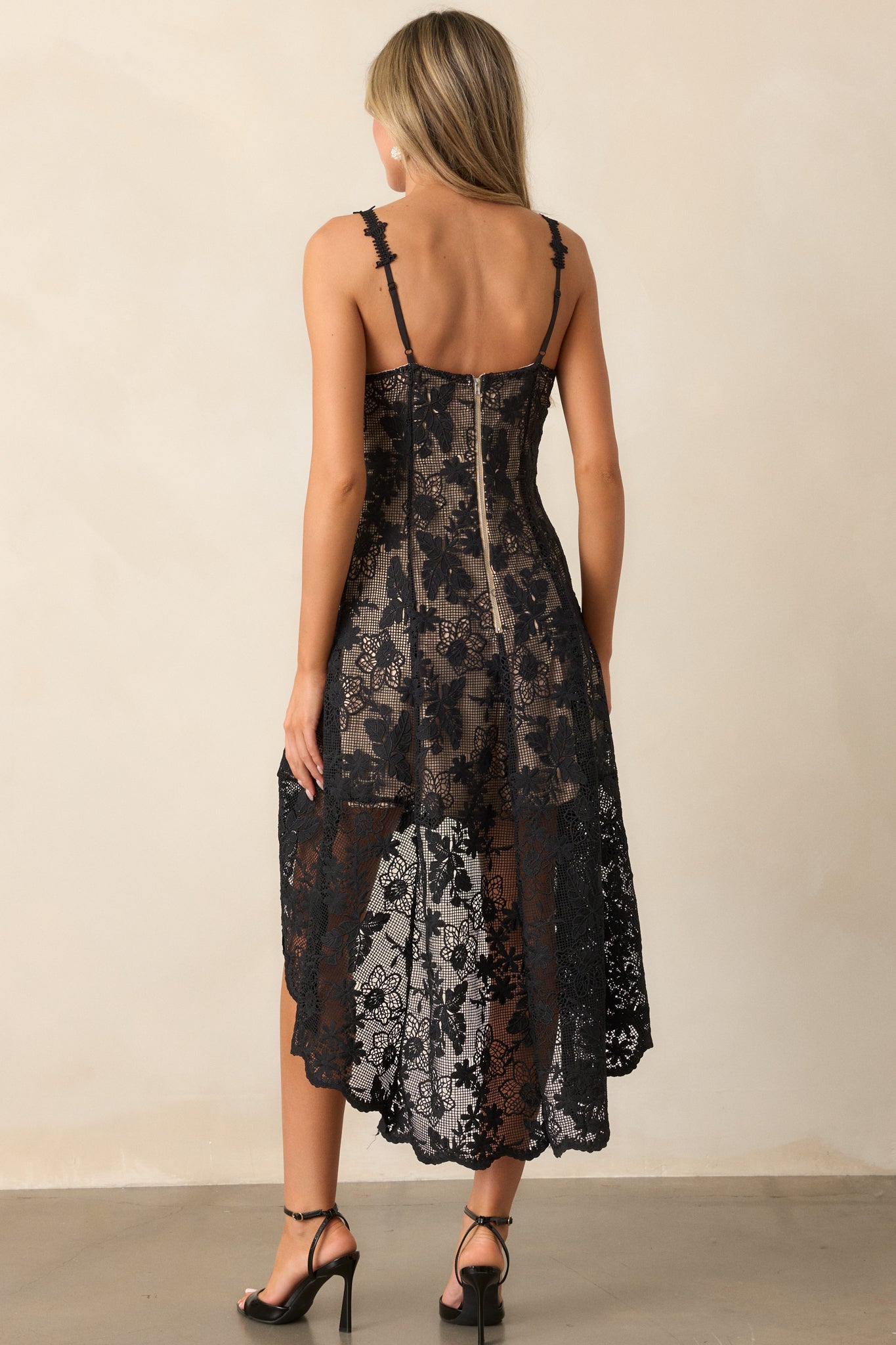 Back view of the black dress showcasing the functional zipper closure and the embroidered lace overlay, with the high-low hemline visible from the back.