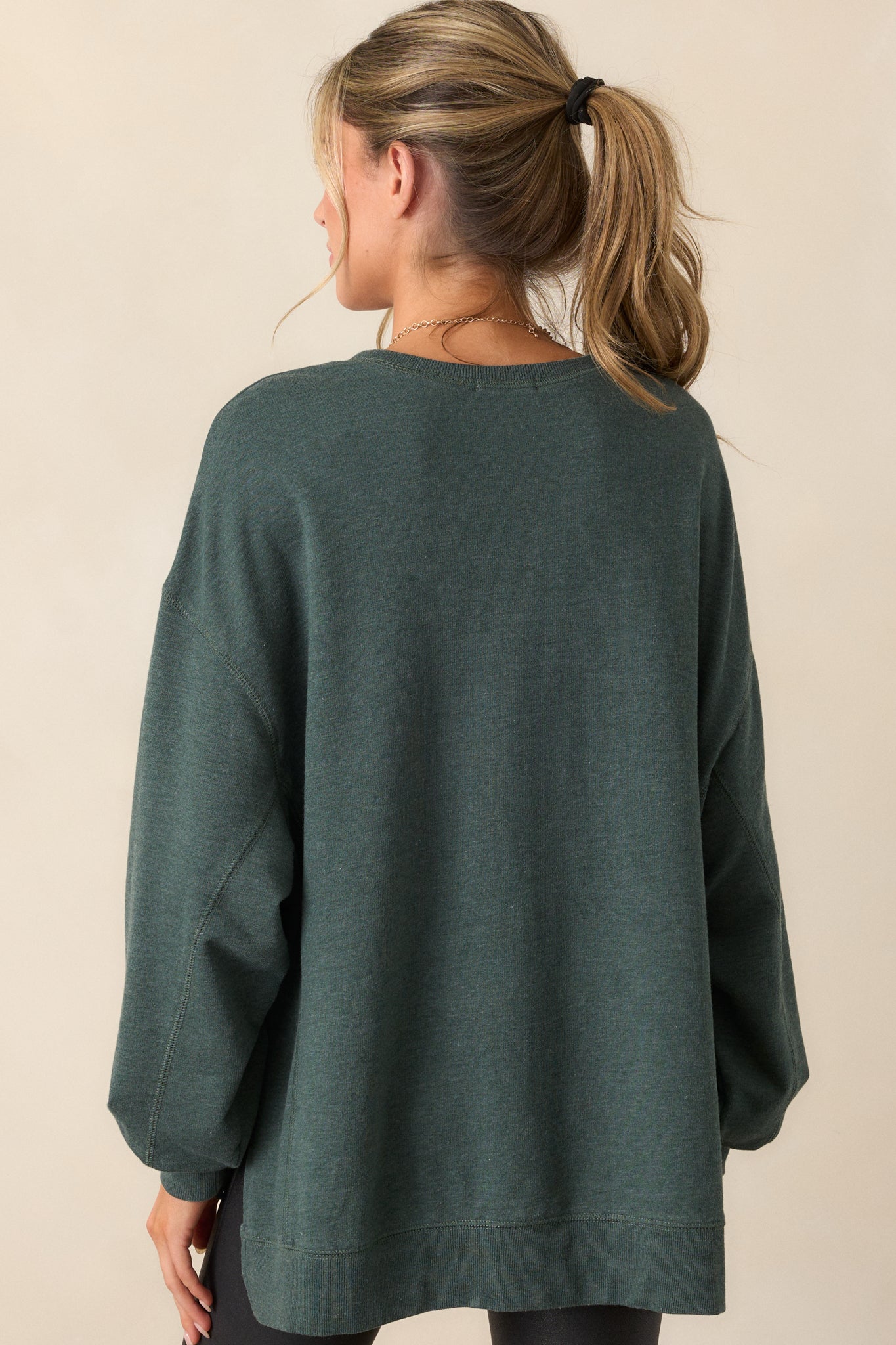 Back view of this top that features a crew neckline, dropped shoulders, ribbed cuffed sleeves, and a high-low split hemline.