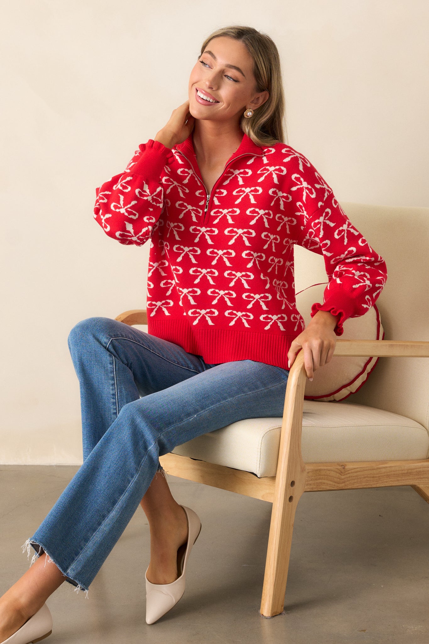 A side view of the red pullover, highlighting the relaxed fit, quarter zip detail, and the ivory bow print, with the ruffled cuffs of the long sleeves prominent.