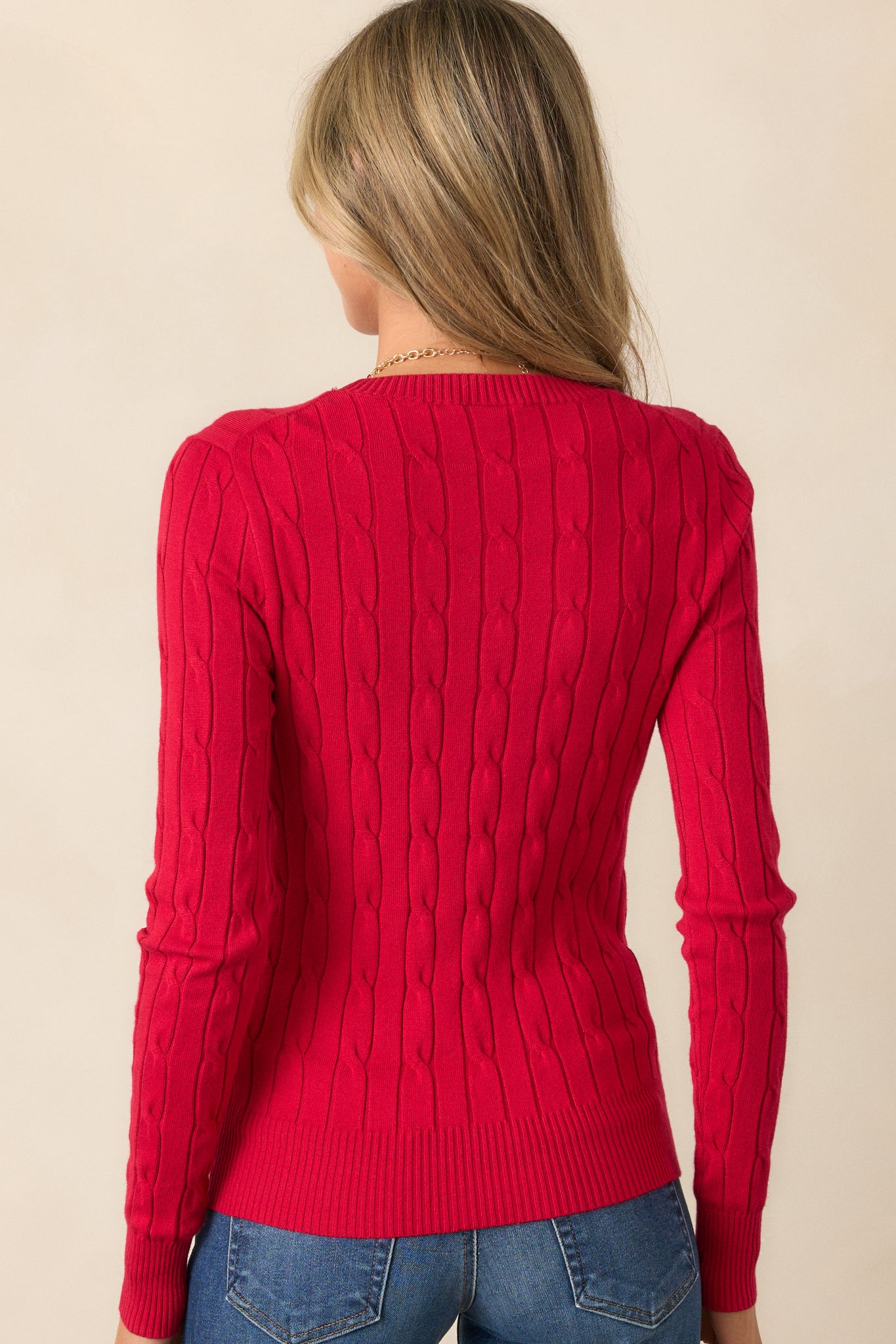 A back view of the bold red sweater highlighting its seamless cable knit design and ribbed hems at the back.