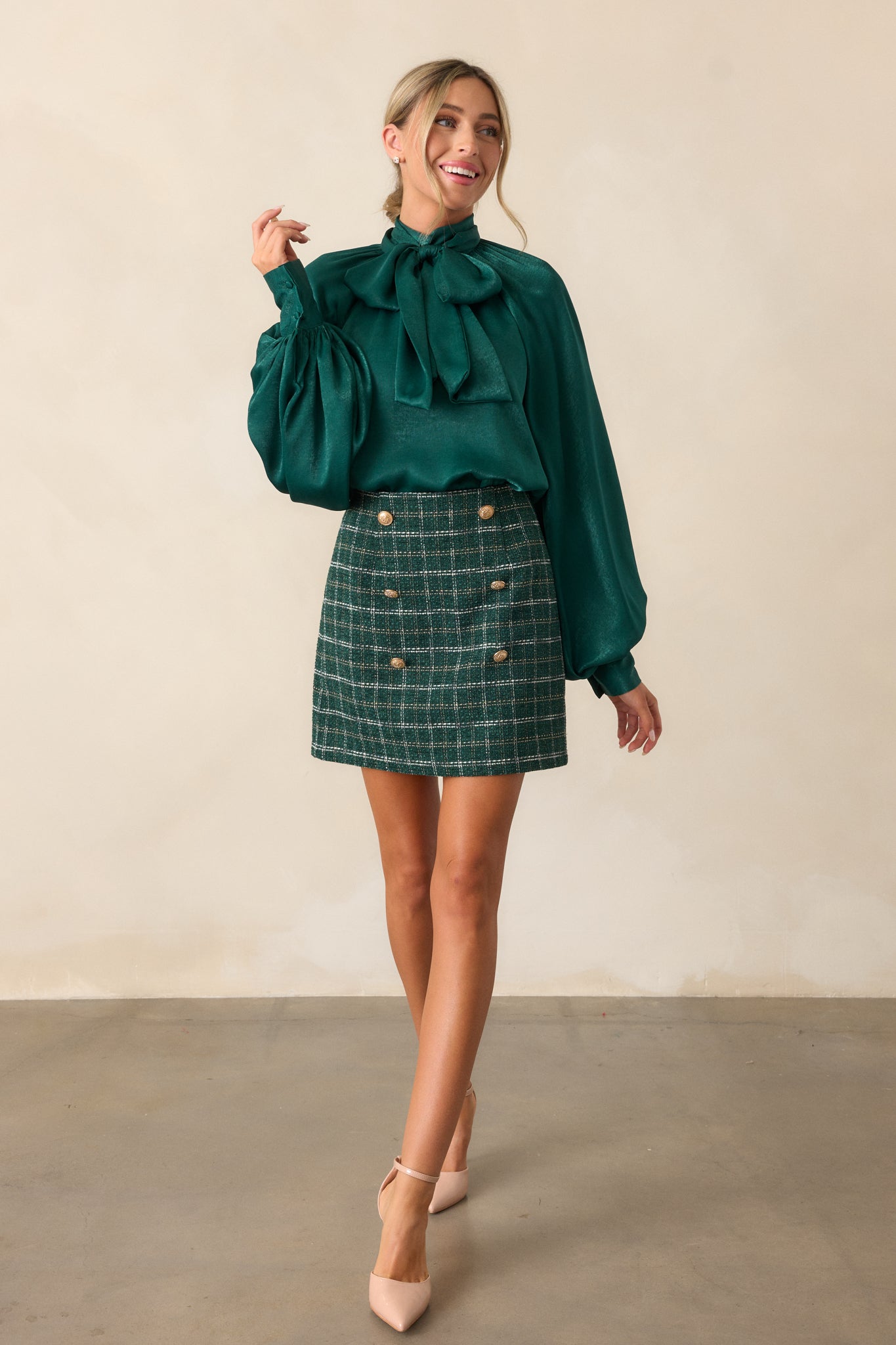 A front view of the green top featuring a high neckline, balloon sleeves with button cuffs, and an adjustable self-tie bow at the neck. The top is styled with the bow in the front and a flowy fit.