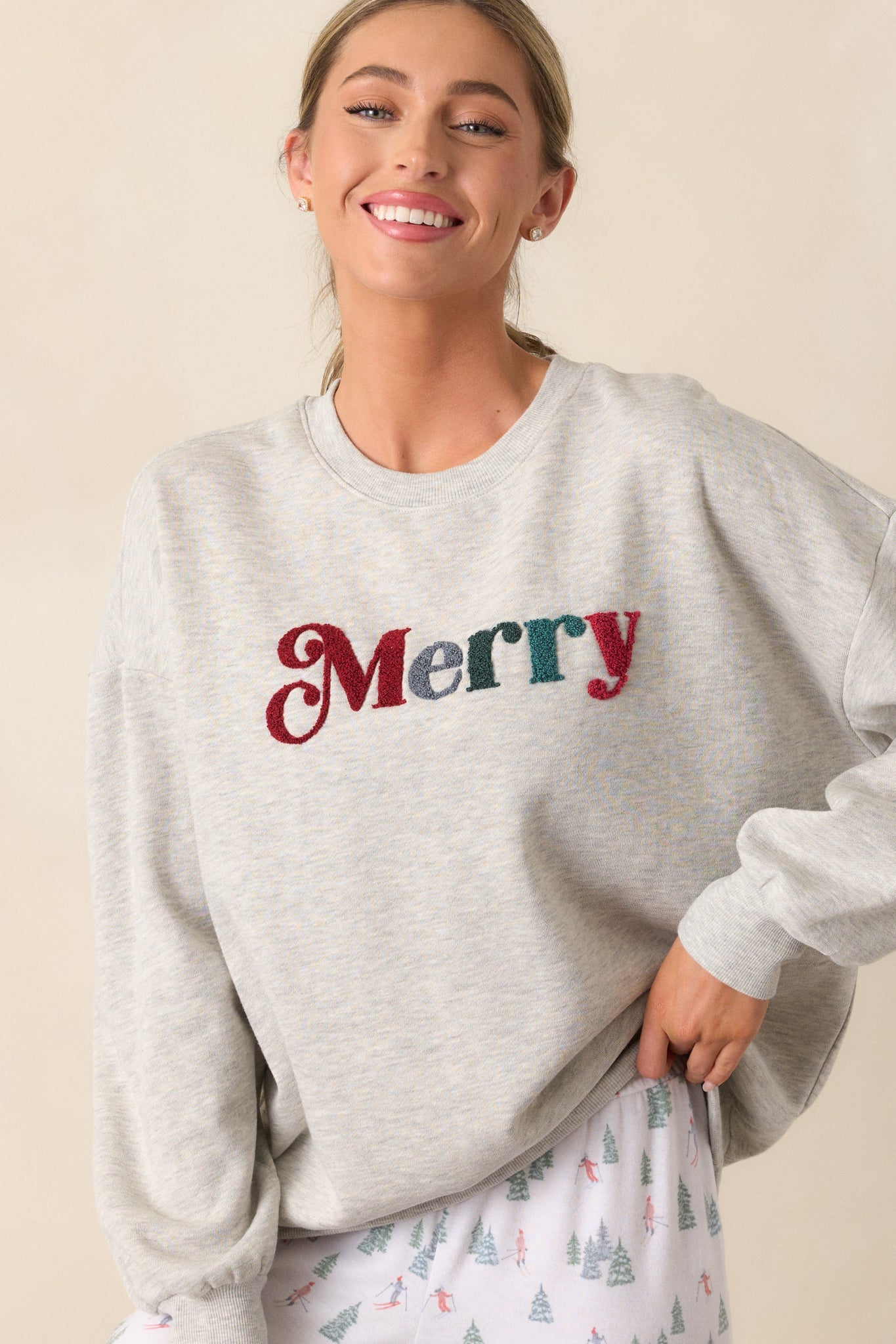 A cropped photo of the ribbed crew neckline and "Merry" detailing on the light heather grey sweatshirt, showcasing the relaxed style and subtle festive touch.