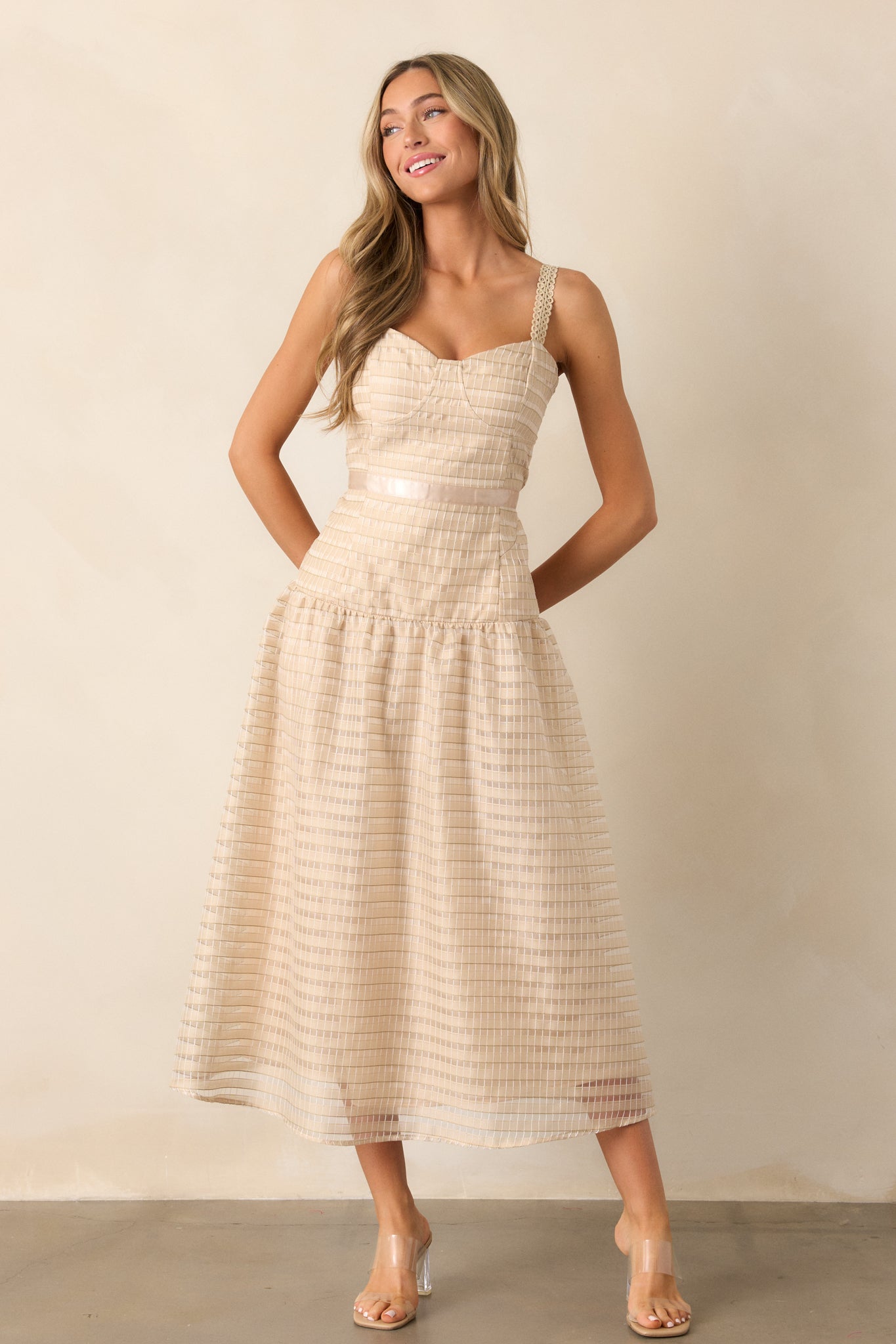 Full body view of a tan dress with a slight sweetheart neckline, showcasing the embroidered detail throughout the bodice and skirt. The dress features a ribbon waist detail, drop waist design, and a fluffy, embroidered skirt that creates a voluminous look.