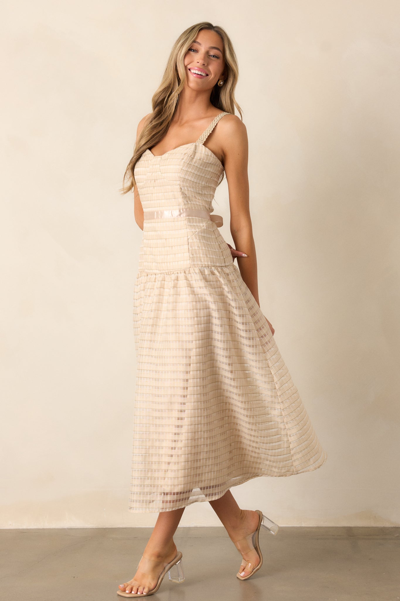 Full body view of a tan dress with a sweetheart neckline, embroidered details, ribbon waist, and a fluffy skirt. The dress features adjustable embroidered straps and a drop waist design.