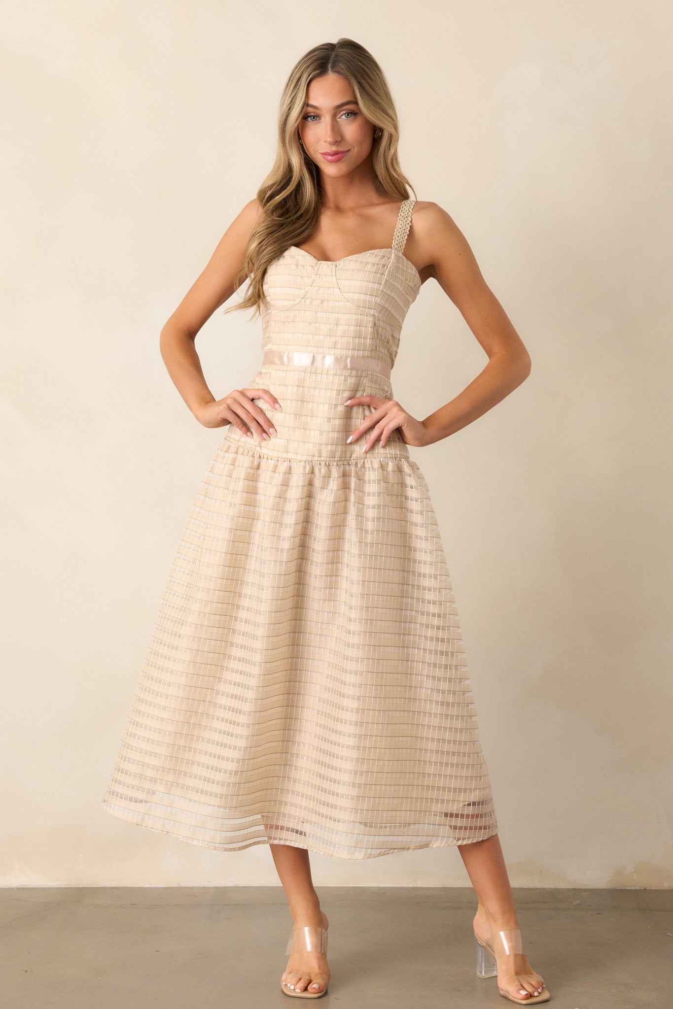 Wide shot of the tan dress, highlighting the slight sweetheart neckline with bust outlining and the beautiful embroidered details that adorn the entire dress. The drop waist and fluffy embroidered skirt are fully visible, with the ribbon waist detailing enhancing the silhouette.