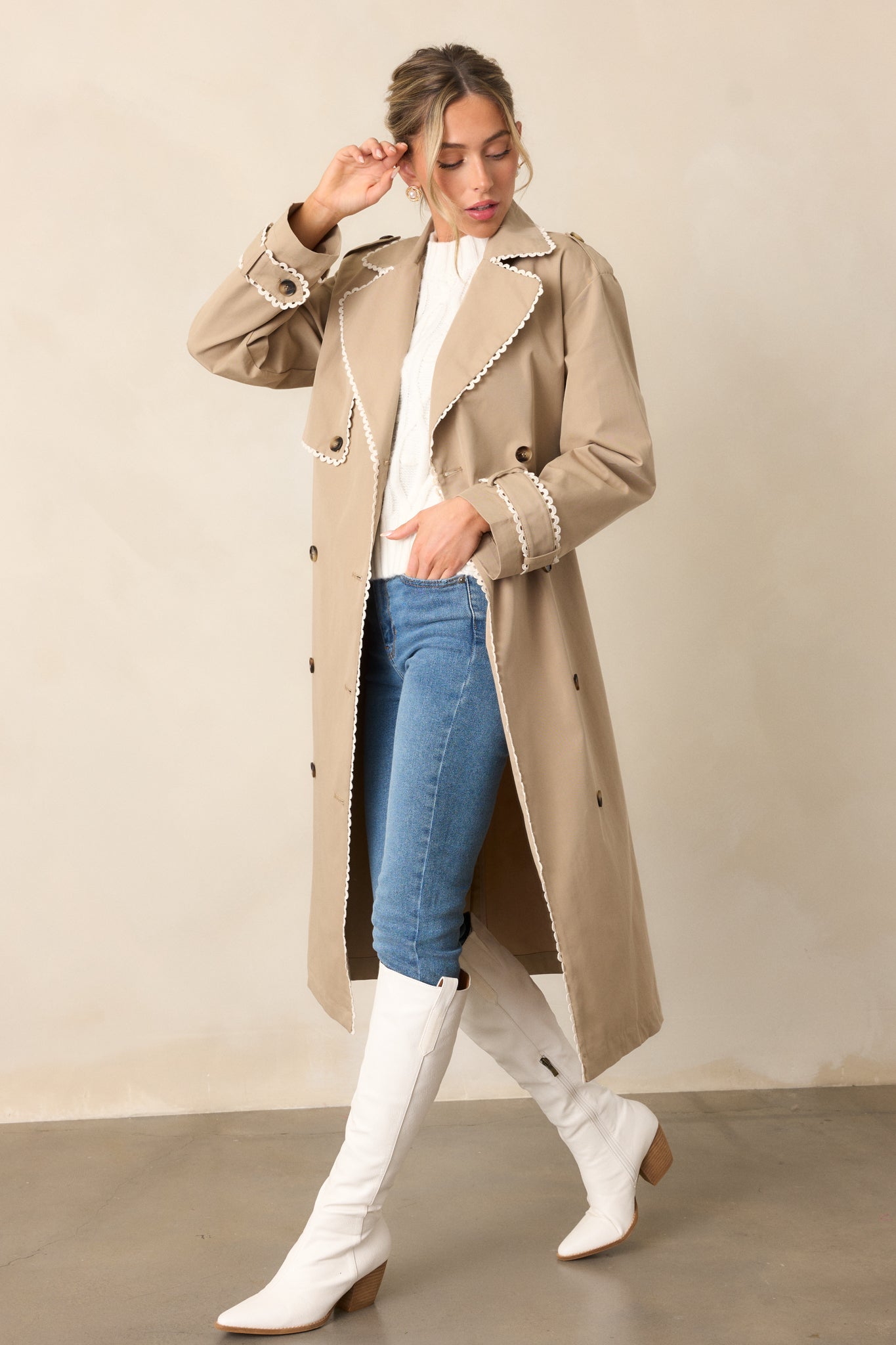 A full view of the taupe trench coat highlighting the eight-button detailing and buttoned cuffs on the long sleeves.