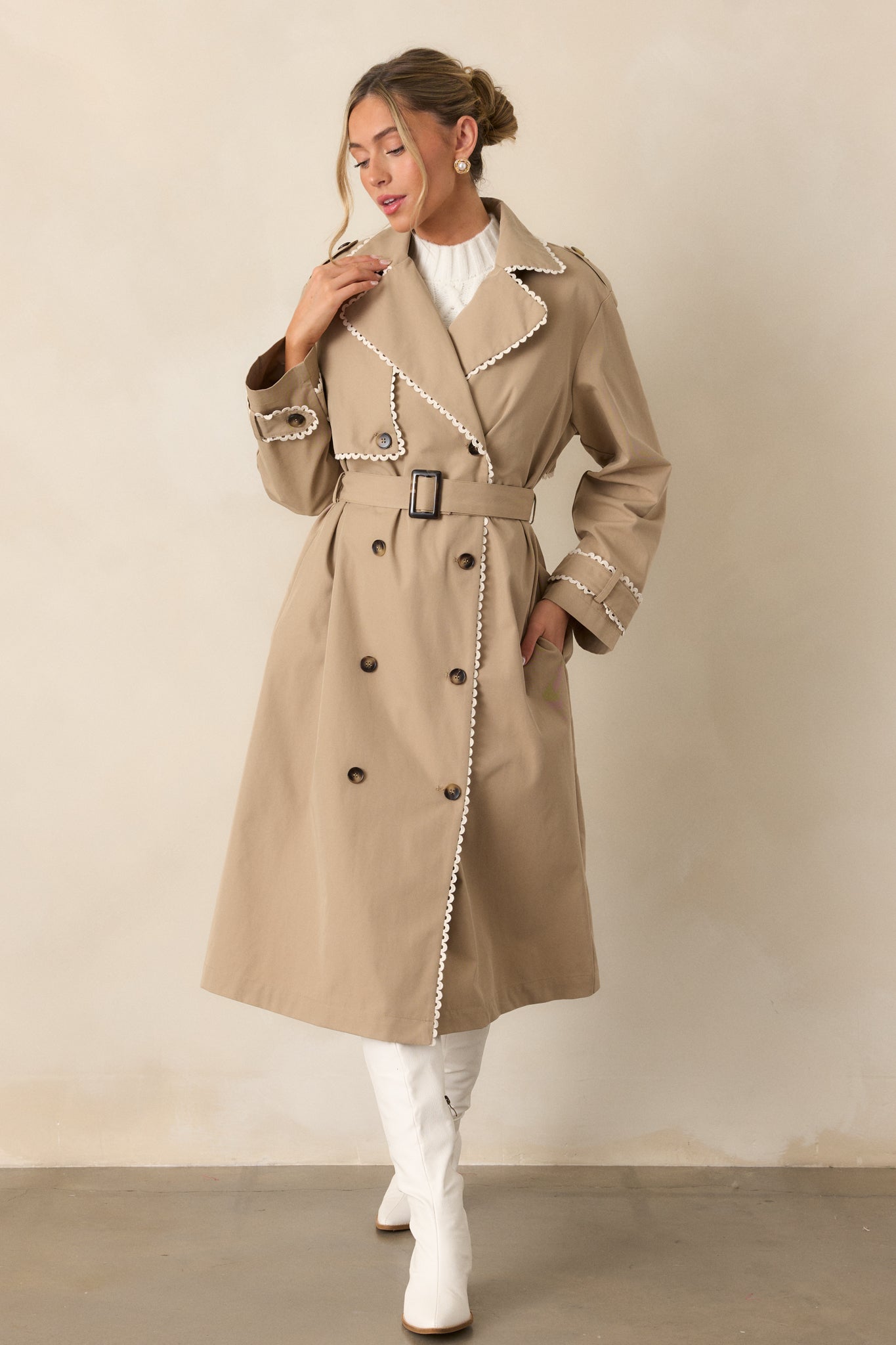 The taupe trench coat displayed with the self-tie waistband fastened neatly at the front, showcasing the ricrac trim.