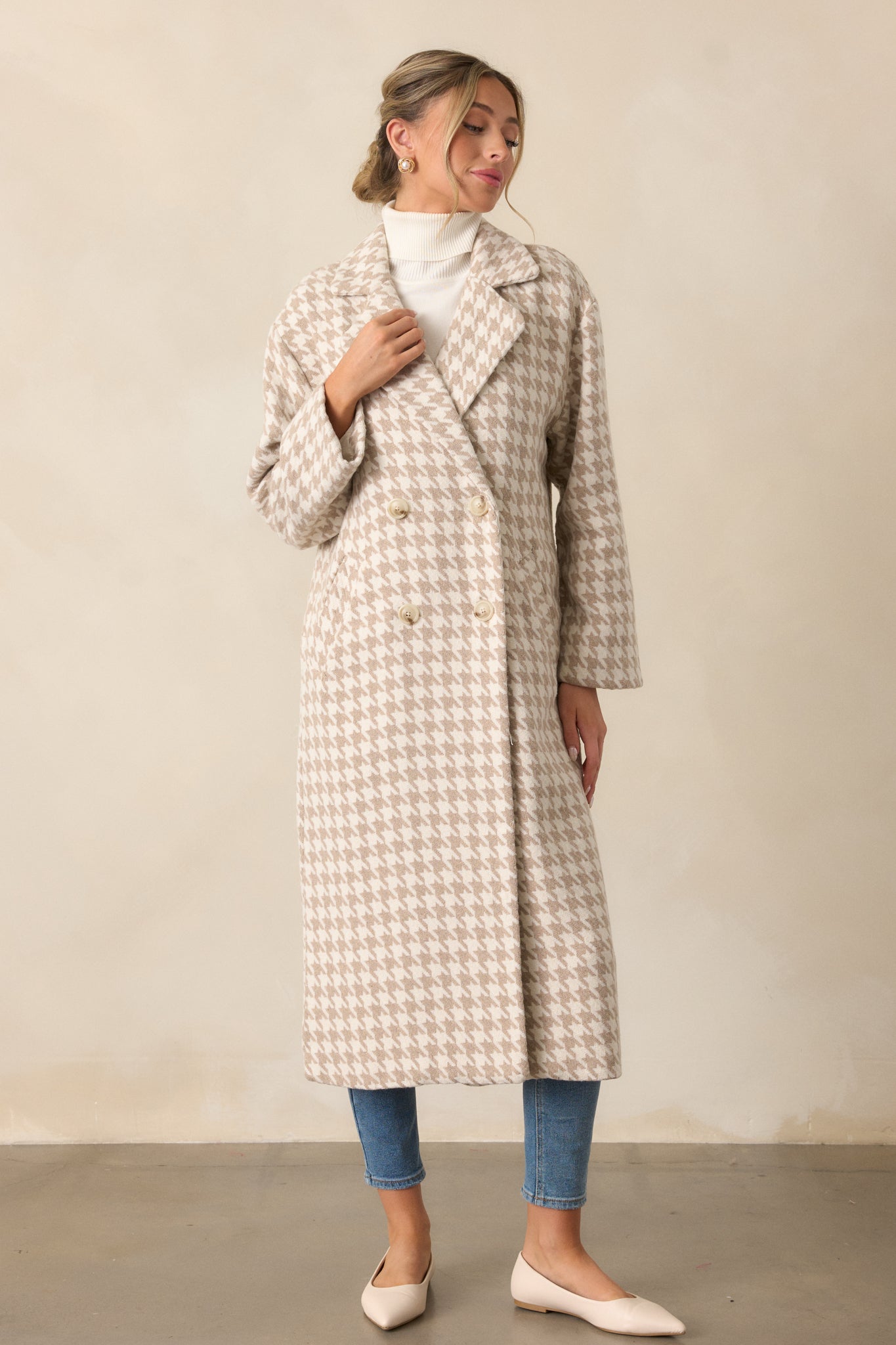 Wide shot of the beige trench coat featuring long sleeves, a lapel neckline, and a button-up front. The houndstooth print and midi length add a classic touch.