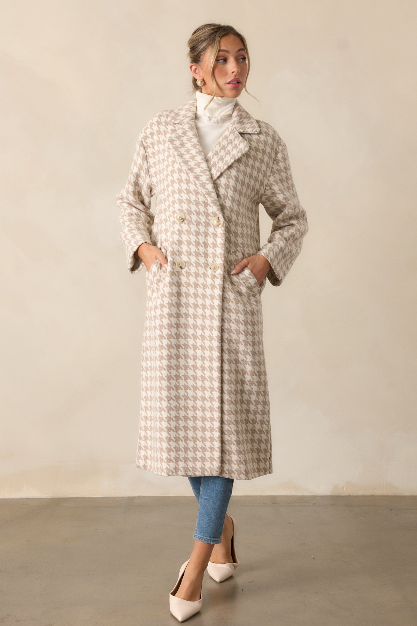 Full-length view of a beige trench coat with a houndstooth print, buttoned front, and lapel neckline. The functional pockets and long sleeves complete the tailored look.