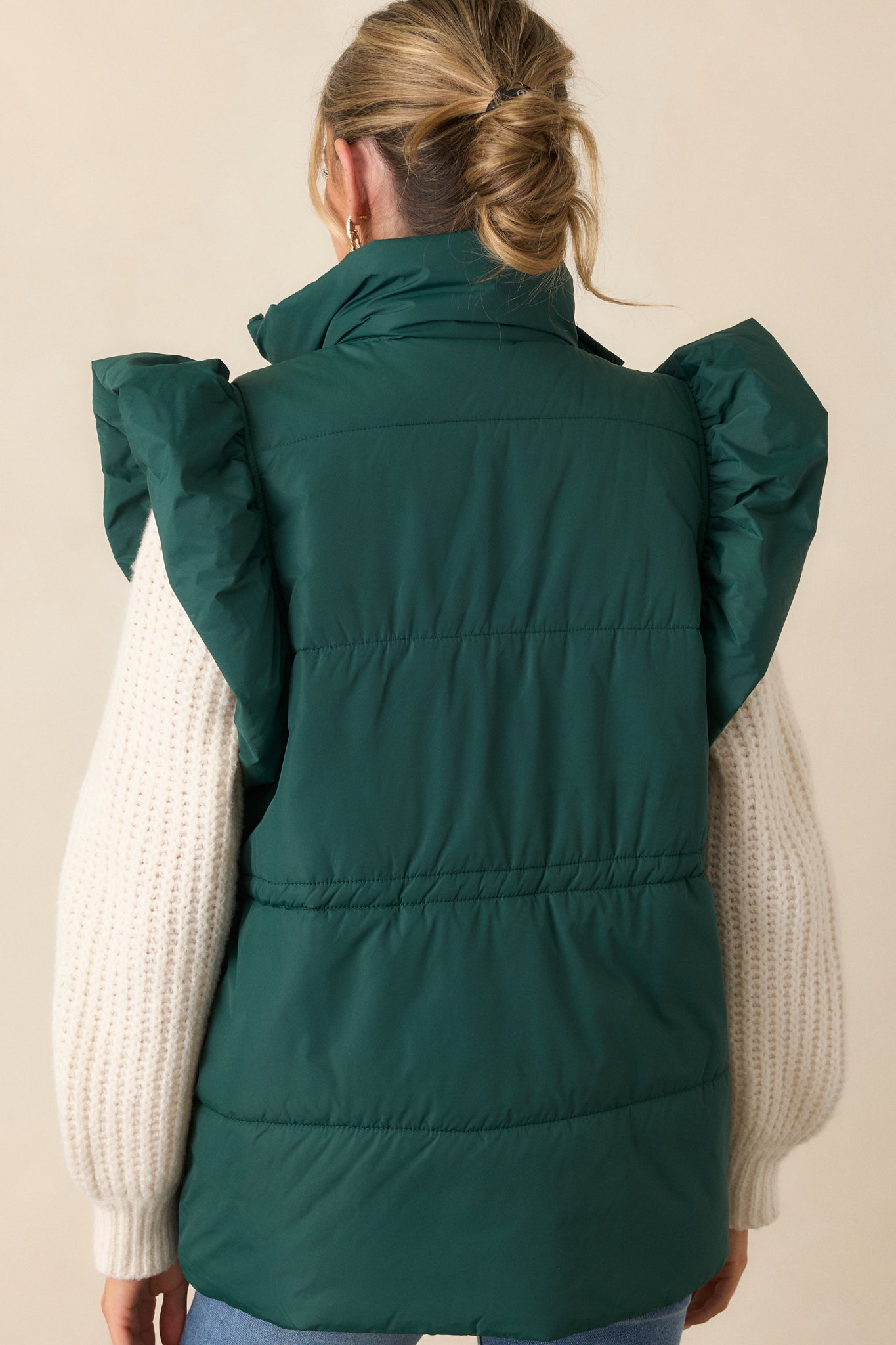 Back view of the forest green puffer vest, highlighting the clean design and showing the fluffy flutter sleeves from behind. The cinched waist and functional hip pockets are subtly visible from this angle.