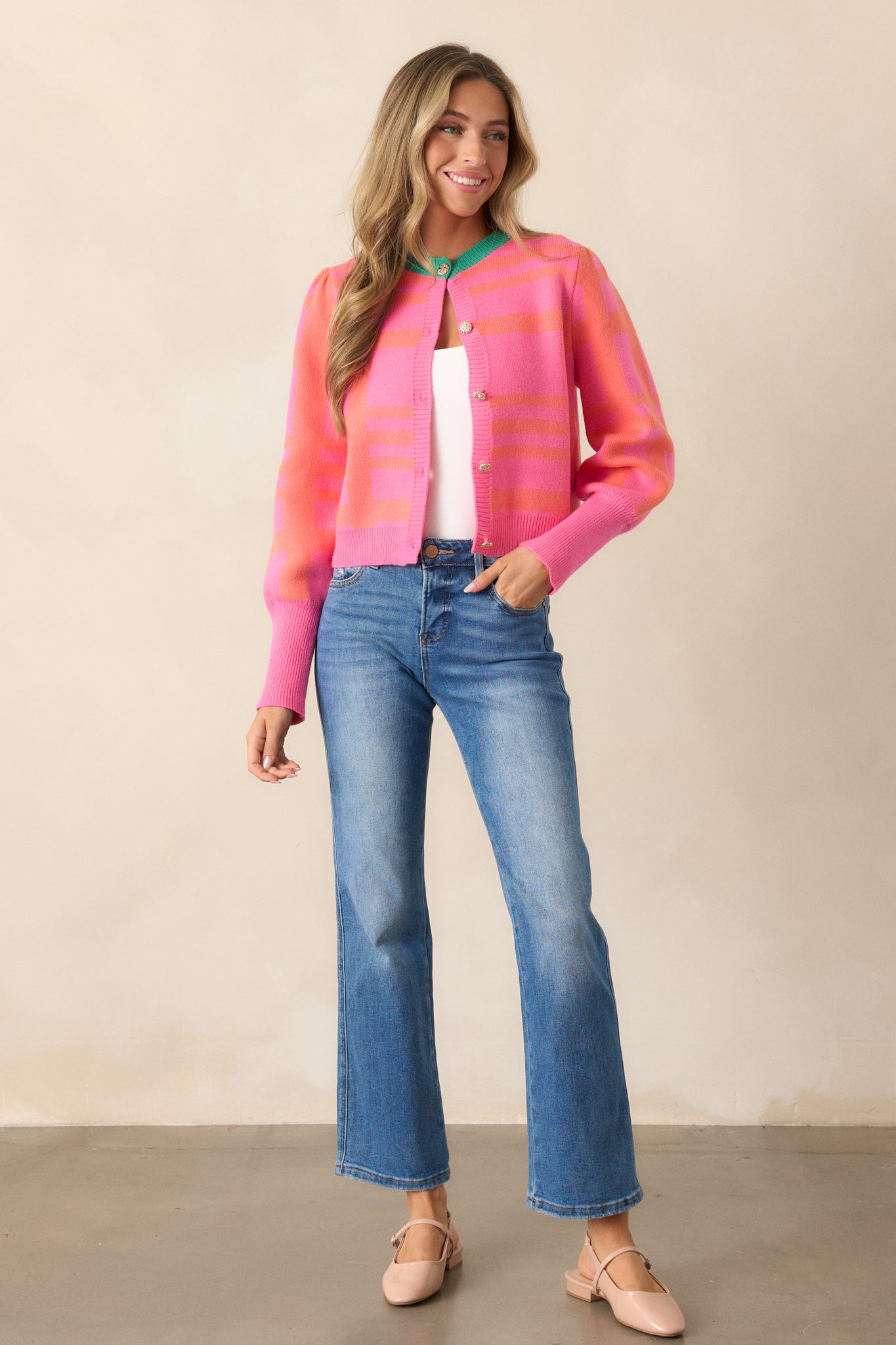 Full view of the pink cardigan, featuring a rounded color-blocked green neckline, orange stripe detailing, and puff sleeves with rib knit cuffs.