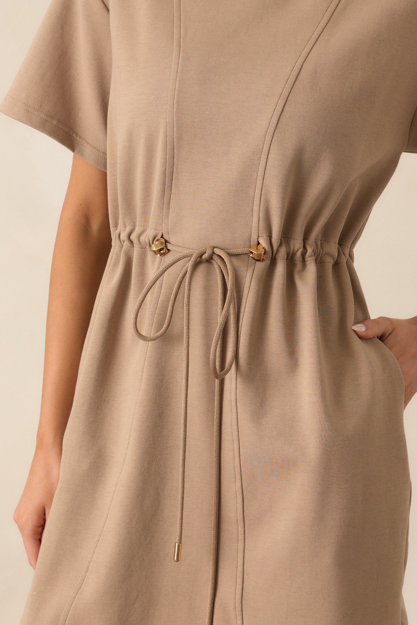 Close-up of the gold heart-shaped charms and gold aglets on the drawstring waist of the light mocha mini dress.