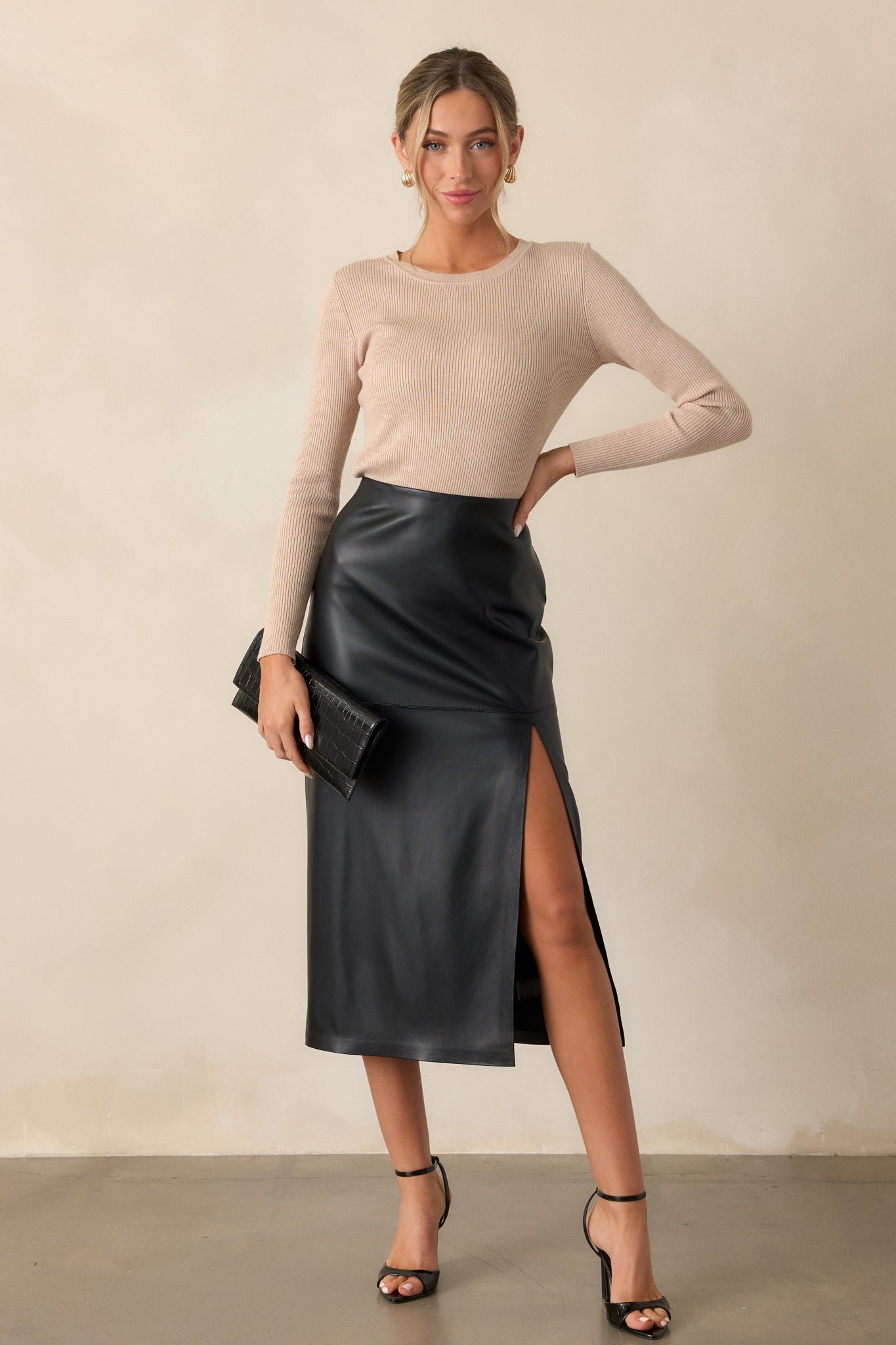 A black midi skirt featuring faux leather paneling and a sleek side slit is displayed in a full-body angled view.