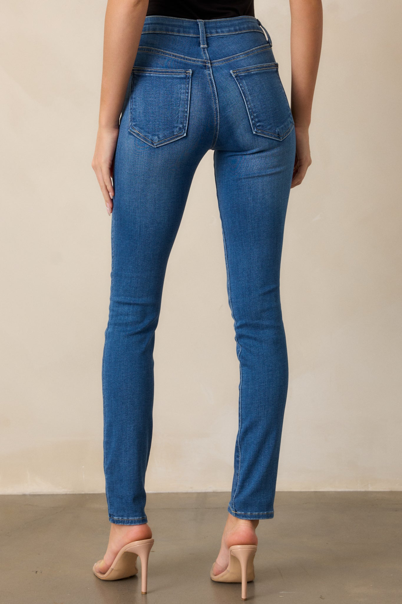 A back view of the medium wash jeans, focusing on the fit around the waist and the back pockets. The high waist and functional belt loops are visible, along with the slim, tailored fit.