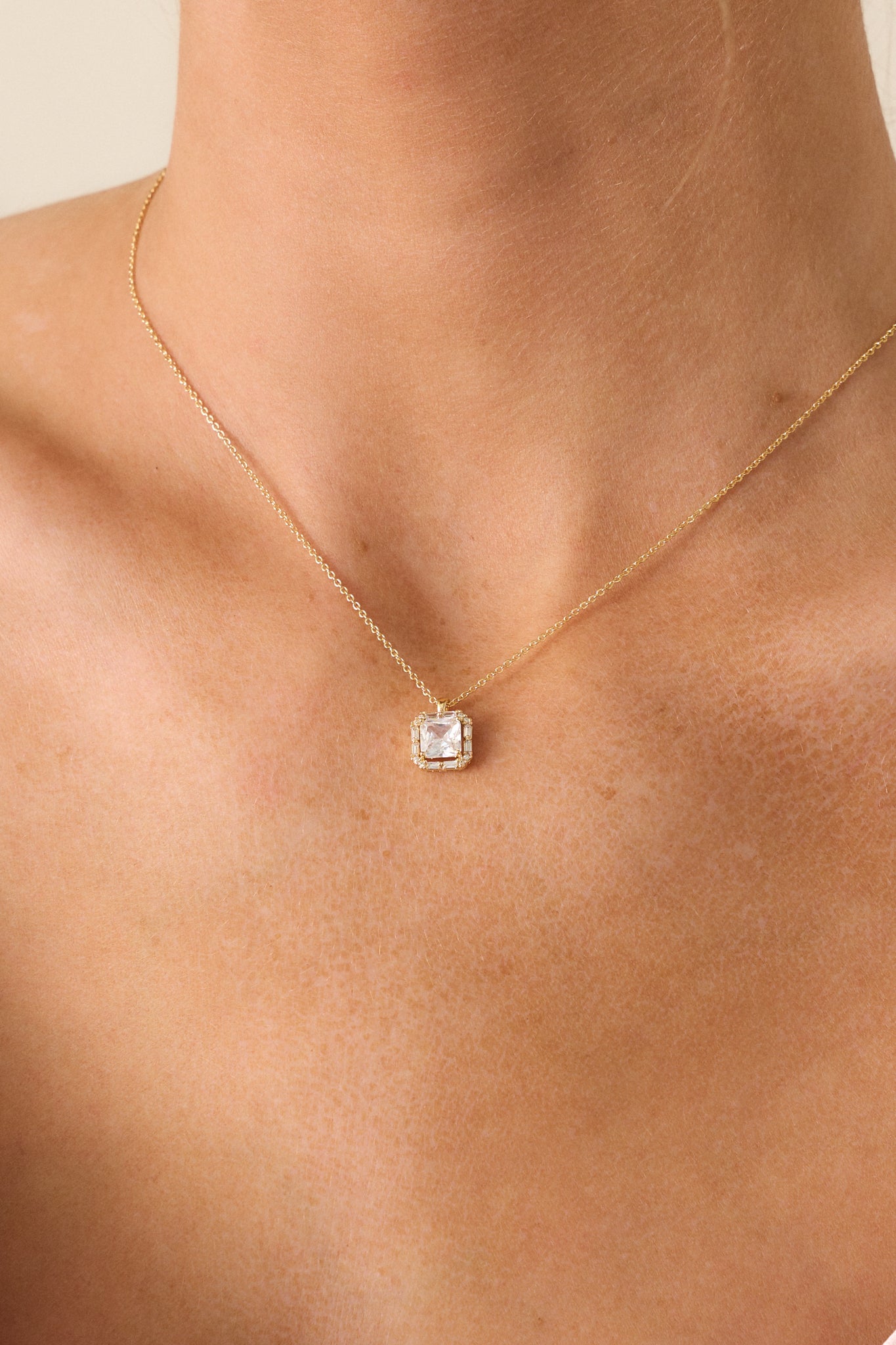 Zoomed-in shot of the small square pendant on the gold necklace, emphasizing the large square rhinestone in the middle and the fine gold chain connecting it