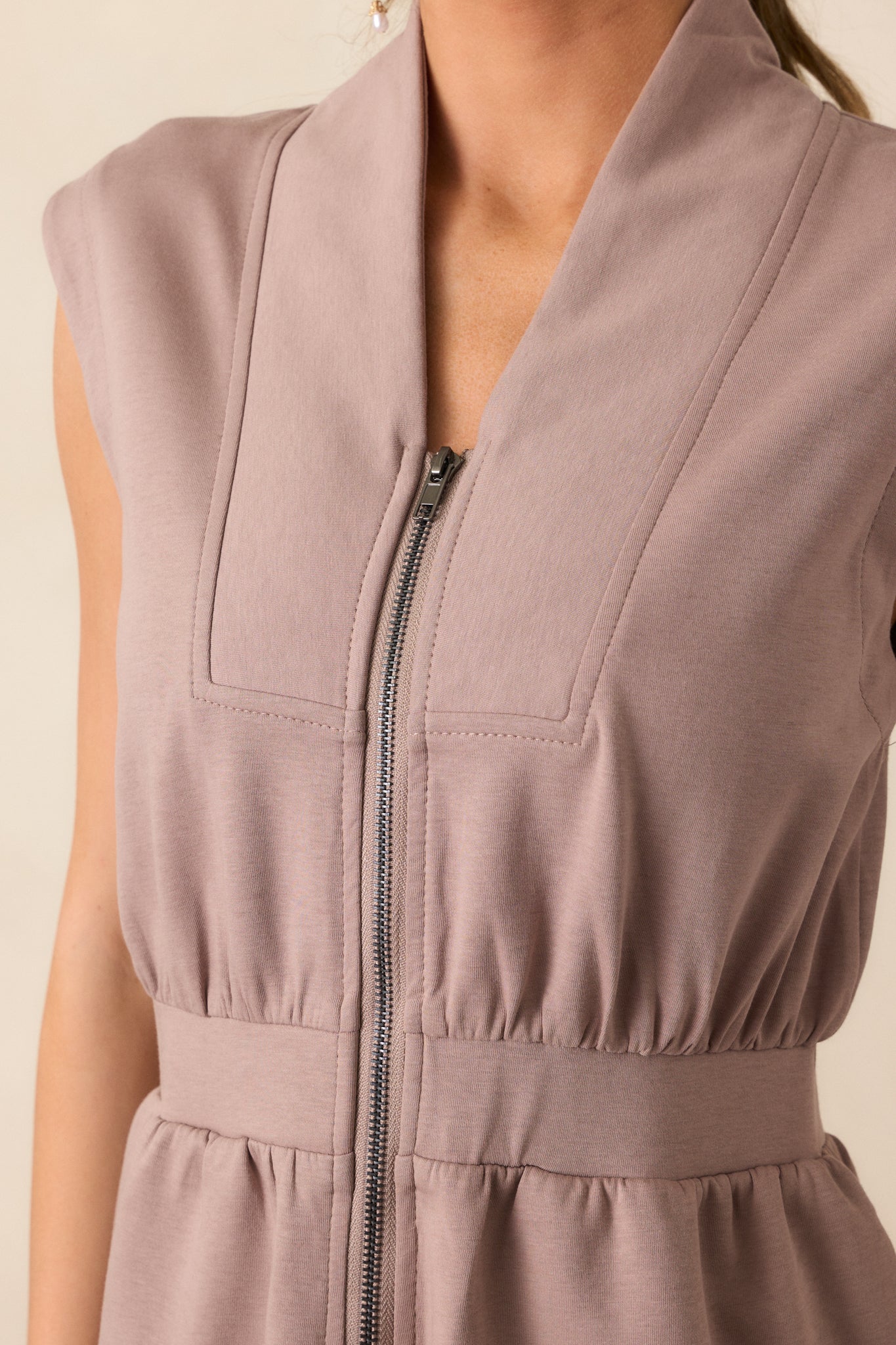 A close-up of the dress showing the V neckline with a slight collar, adding a touch of sophistication. The photo also highlights the functional zip front as well as the elastic waistband that cinches the waist for a flattering fit.