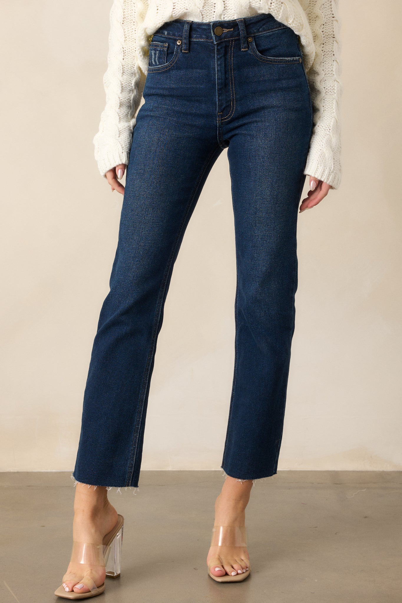 Full length view of dark wash denim jeans with a high-rise waist, scissor cut-off hem, functional pockets, belt loops, and a zipper button closure.