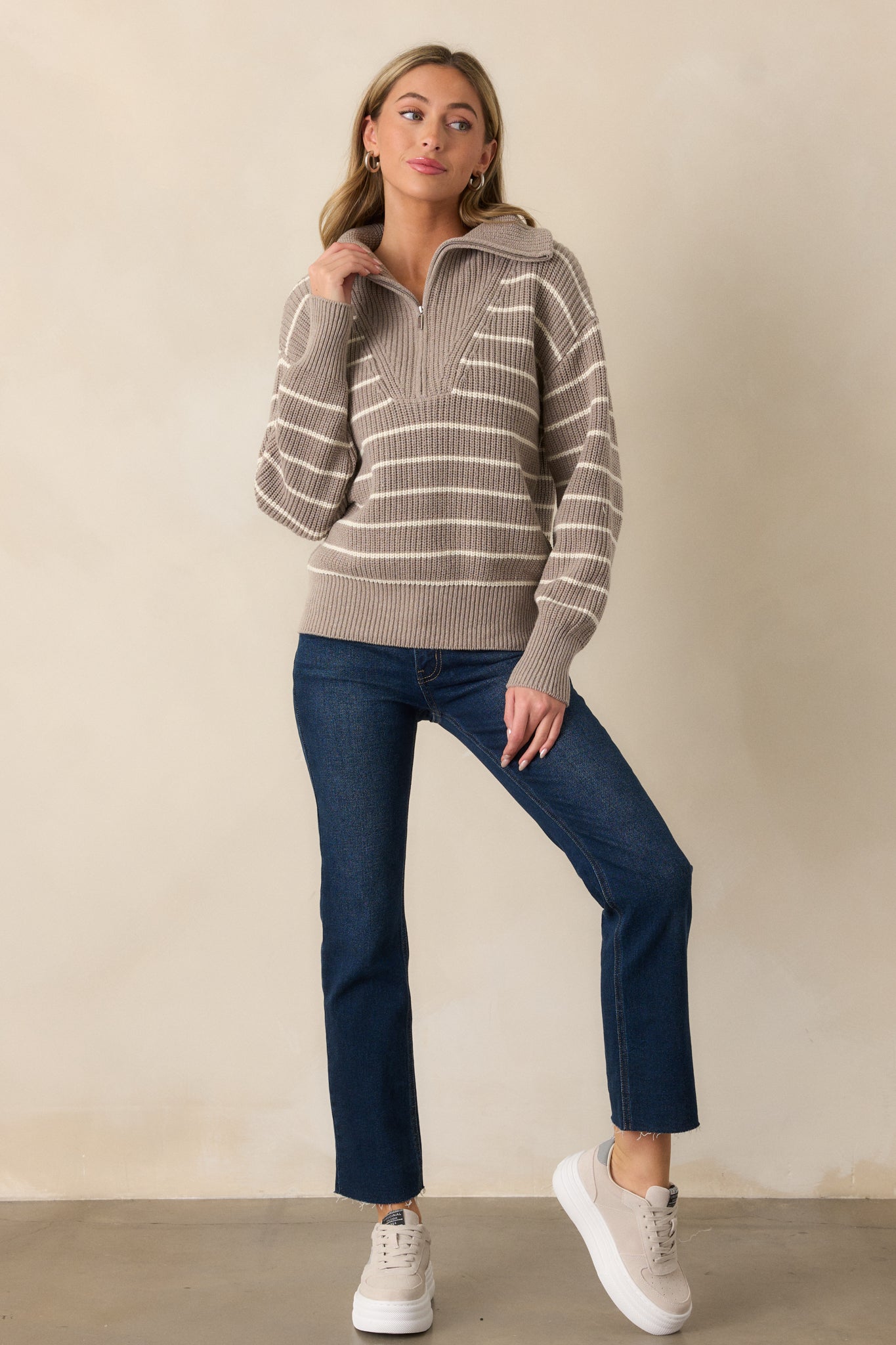 A full-length shot of a heather taupe sweater with an oversized collar and a half zip front. The sweater is designed with an ivory stripe pattern and rib knit hems, paired with long sleeves for a warm, fashionable appearance.