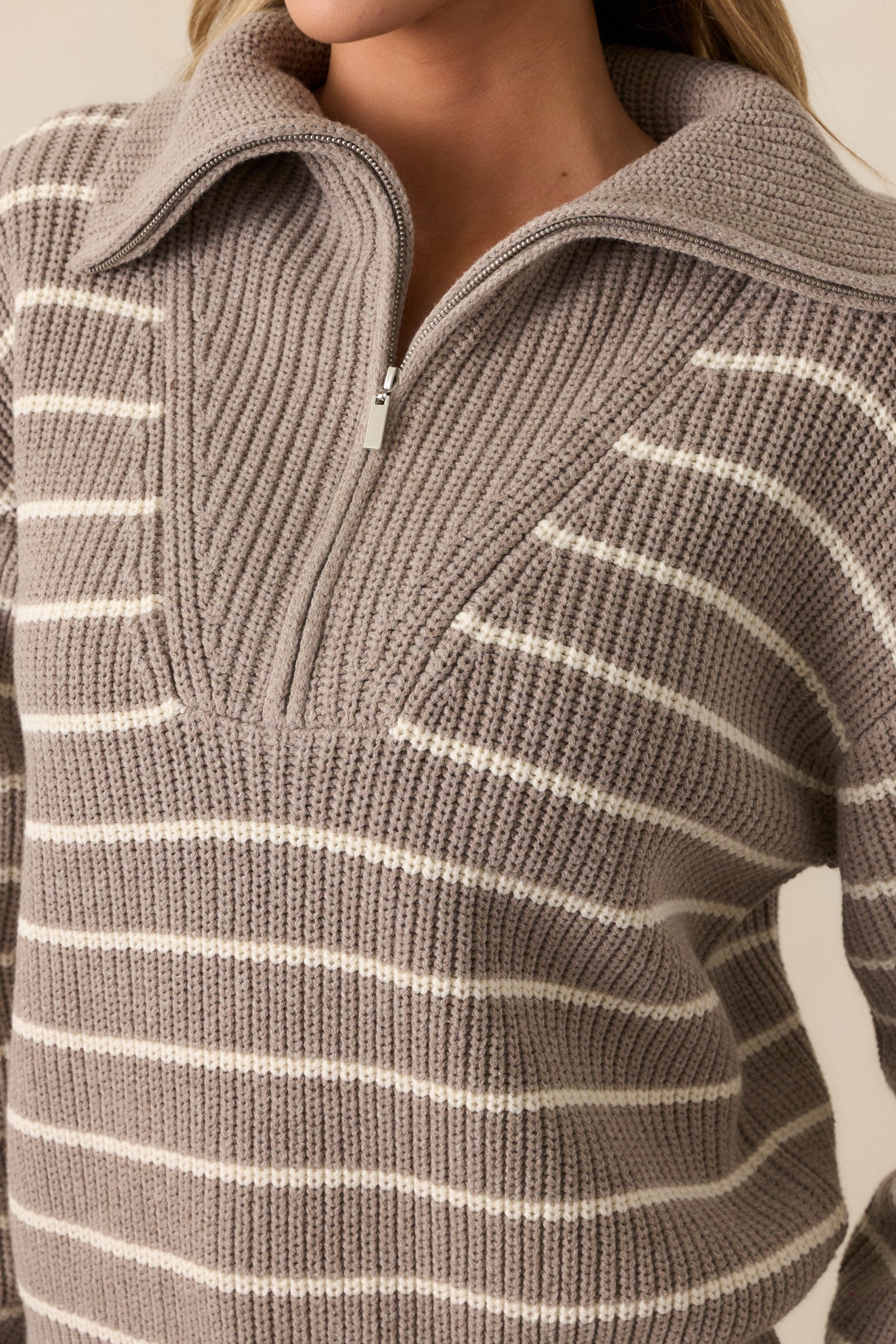 A close-up of the heather taupe sweater’s oversized collar neckline and functional half zip front. The ivory stripe pattern and rib knit hems are clearly visible, adding texture and style to the top.