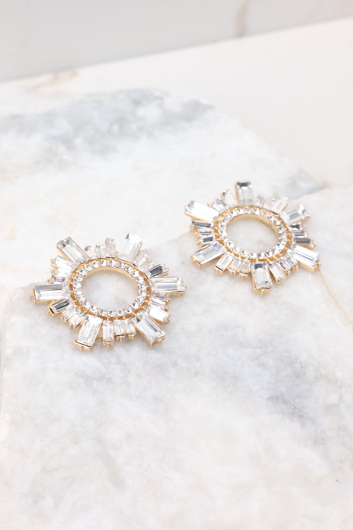 Side view of these earrings that feature gold hardware, a circular design, rhinestone detailing, and a secure post backing.