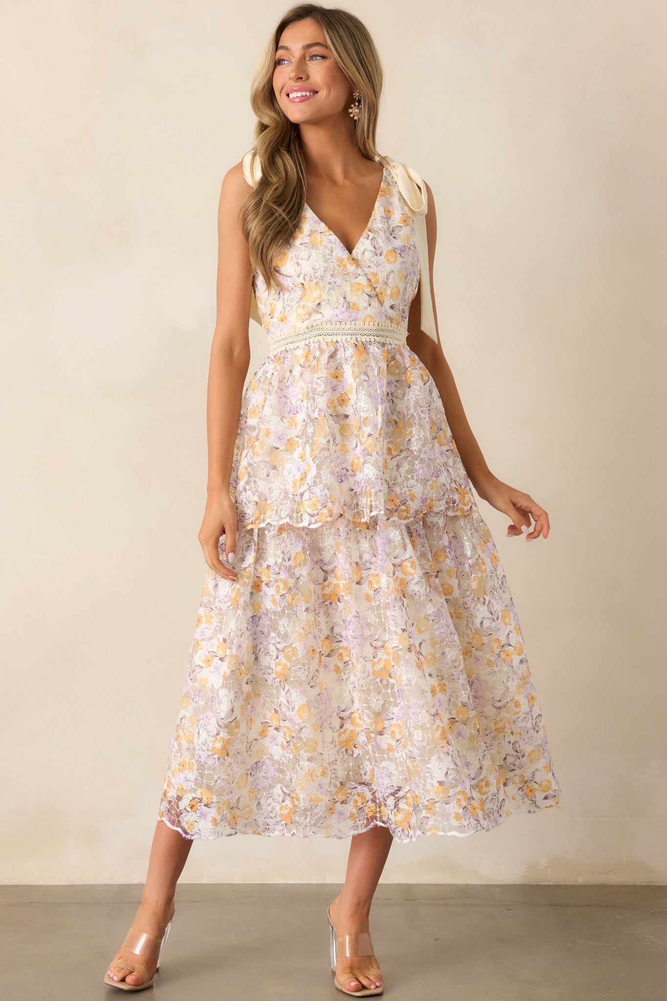 An apricot midi dress with a v-neckline, ribbon shoulder ties, and a floral embroidered pattern that adds a soft, feminine touch.