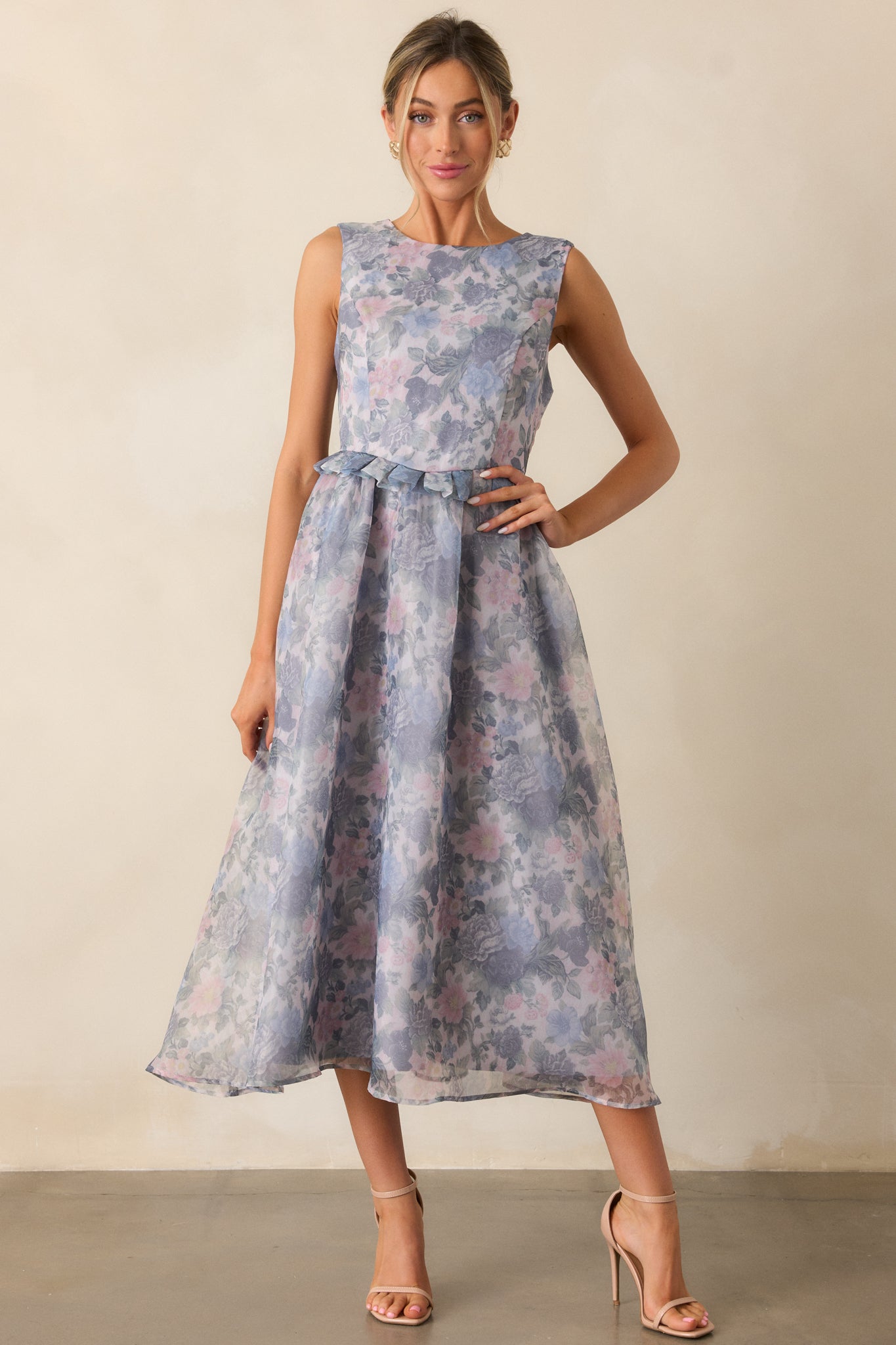 A full body shot emphasizing the feminine silhouette of the dress, featuring the ruffle peplum waistband, floral detailing, and the gentle fall of the midi skirt in an ash blue tone.